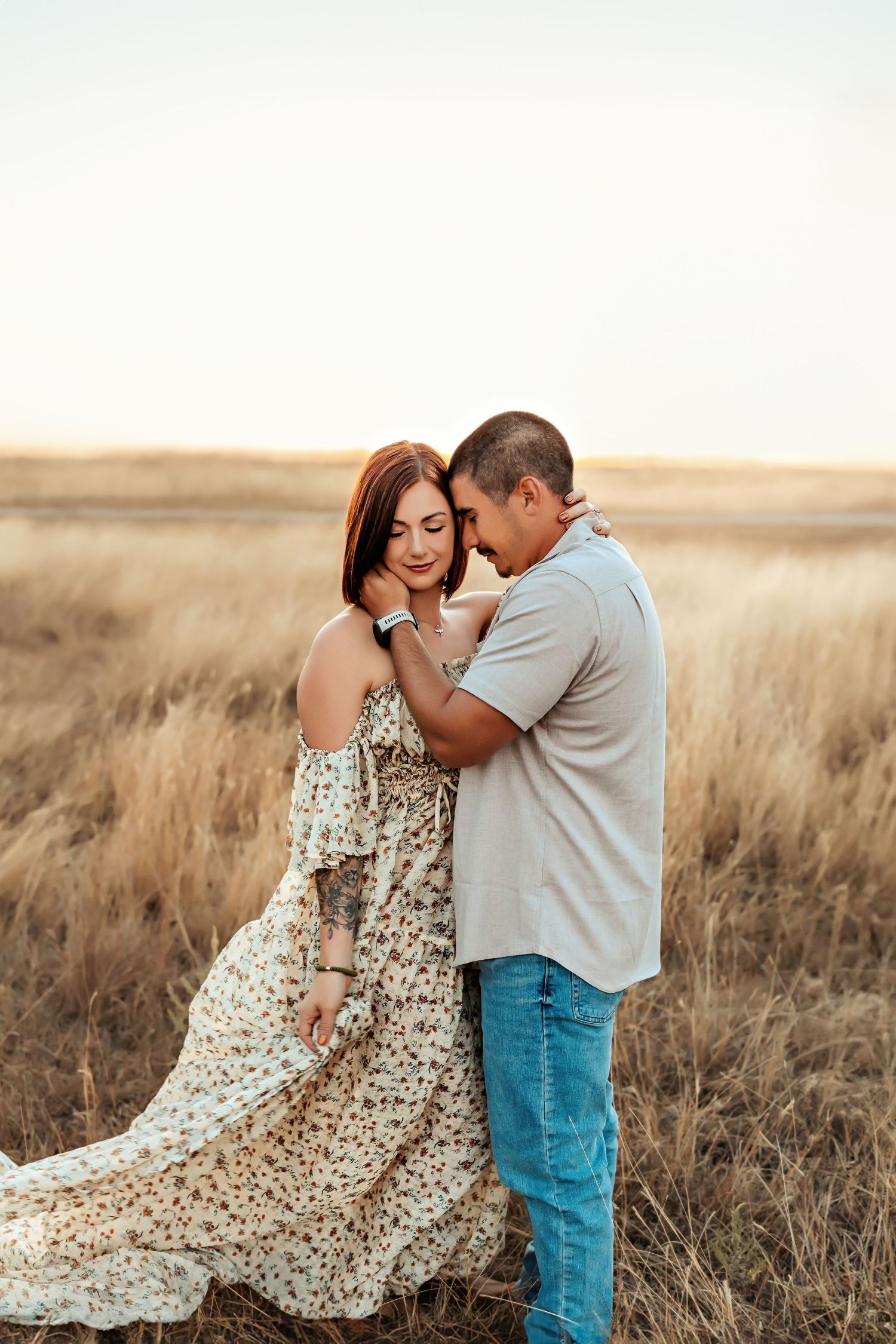 Romantic couple embracing in field with woman wearing flowing floral maxi dress.