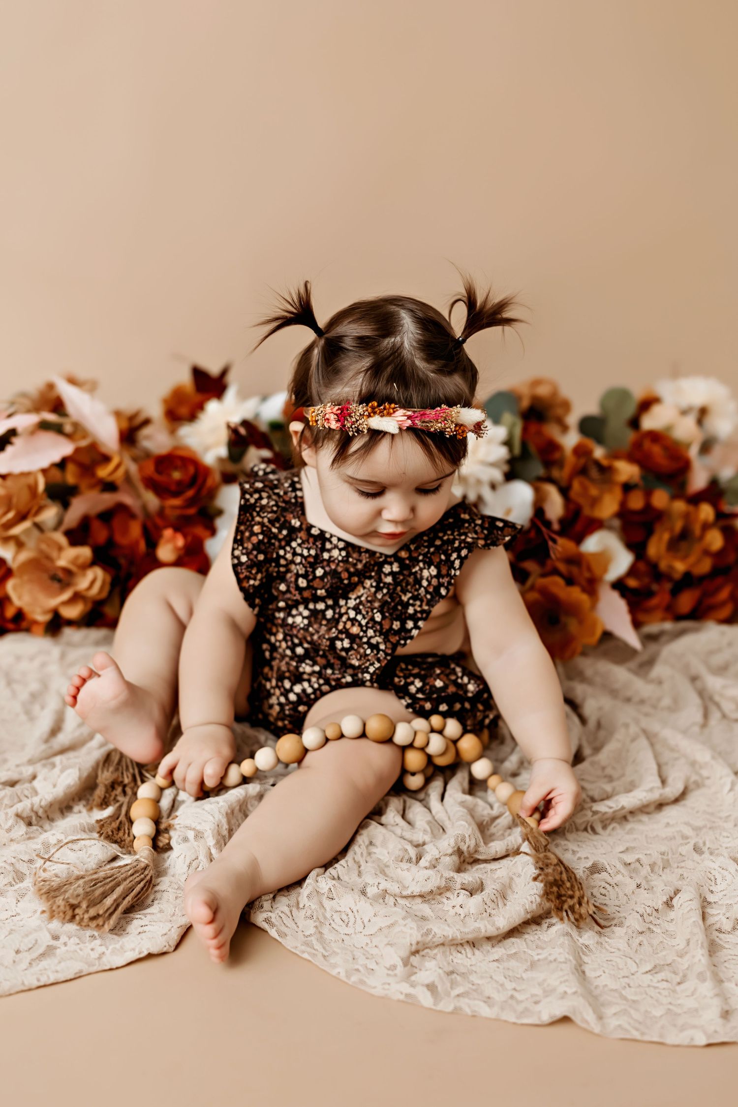 Baby in floral dress with pigtails sitting among autumn decorations.