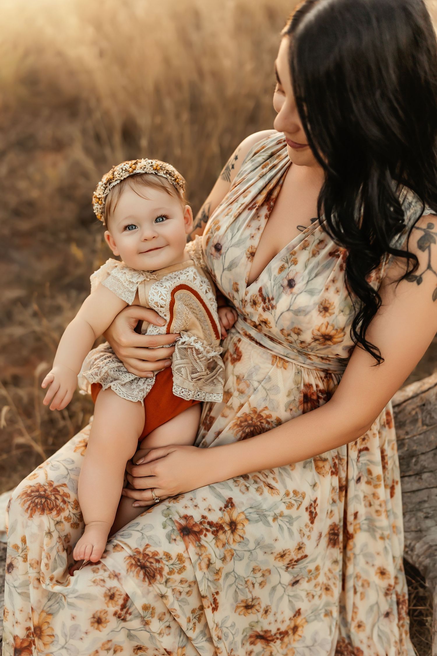 Mother and baby in matching floral dresses pose for outdoor portrait in golden light.