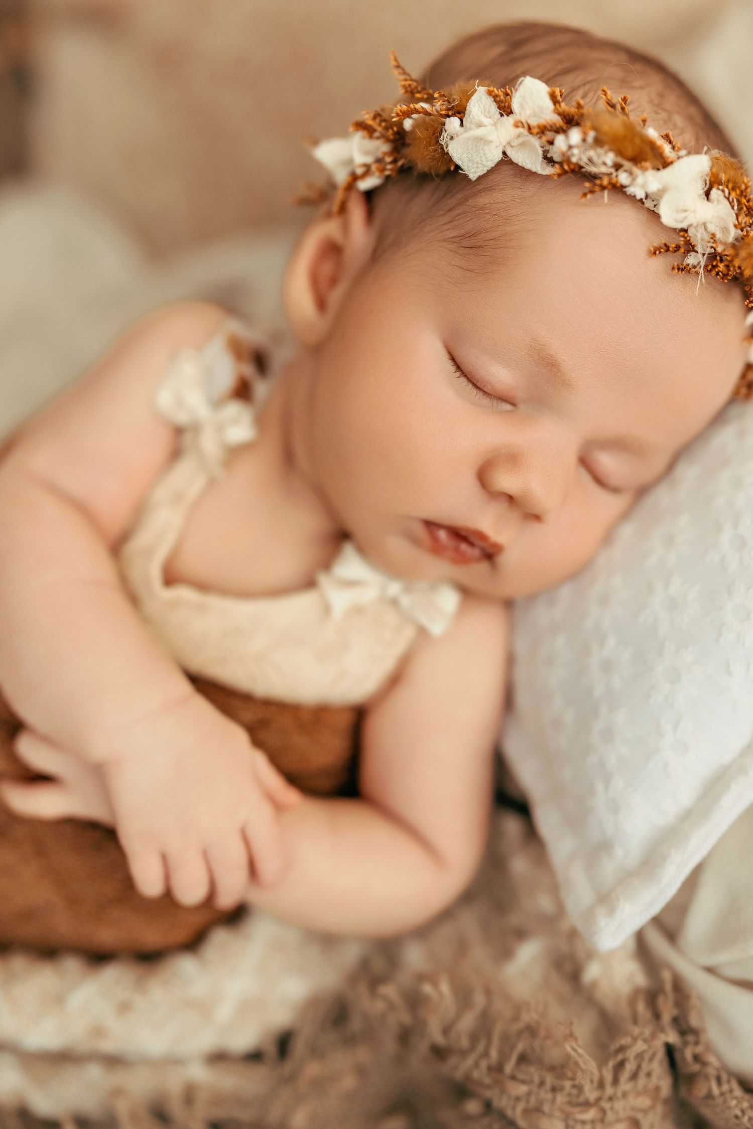 Sleeping newborn in cream outfit with floral crown during professional portrait session.