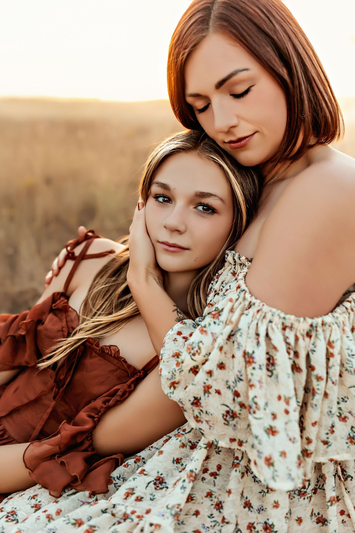 Intimate portrait of two people embracing in floral dresses during golden hour photoshoot.