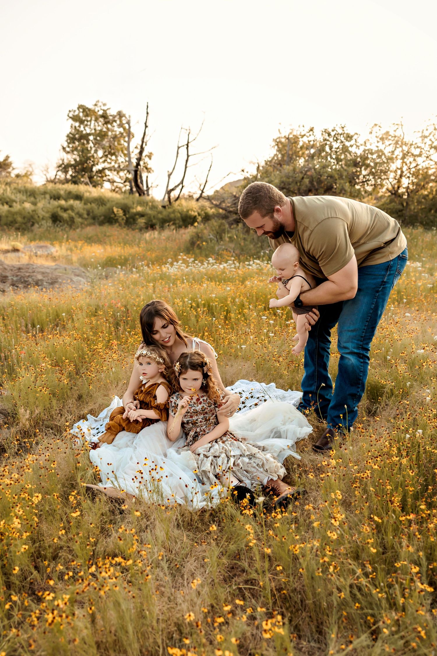 A family enjoys a sunset picnic together on a blanket in a golden wildflower field during summer.