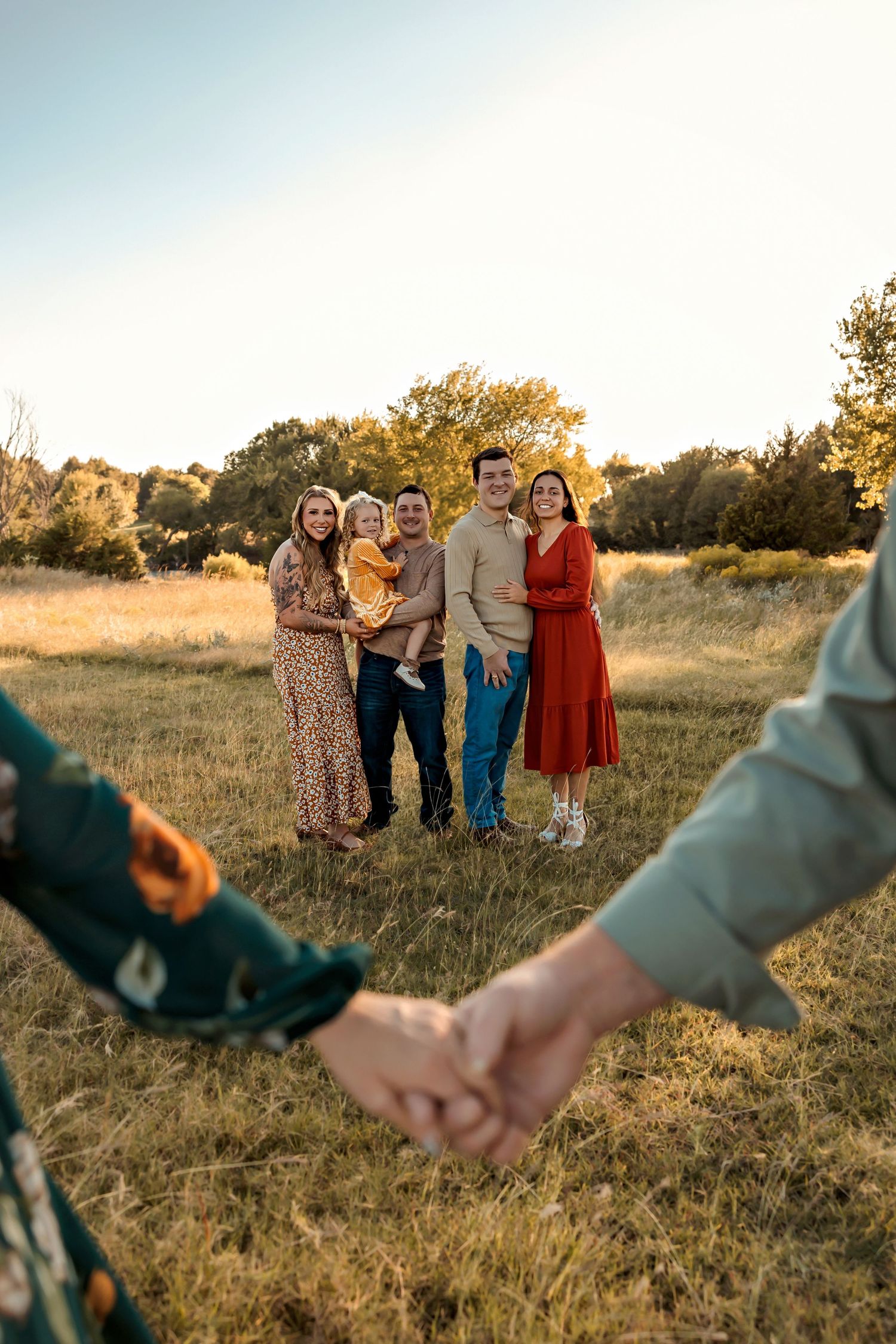 Group of people standing in a golden field at sunset while two hands hold in the foreground.