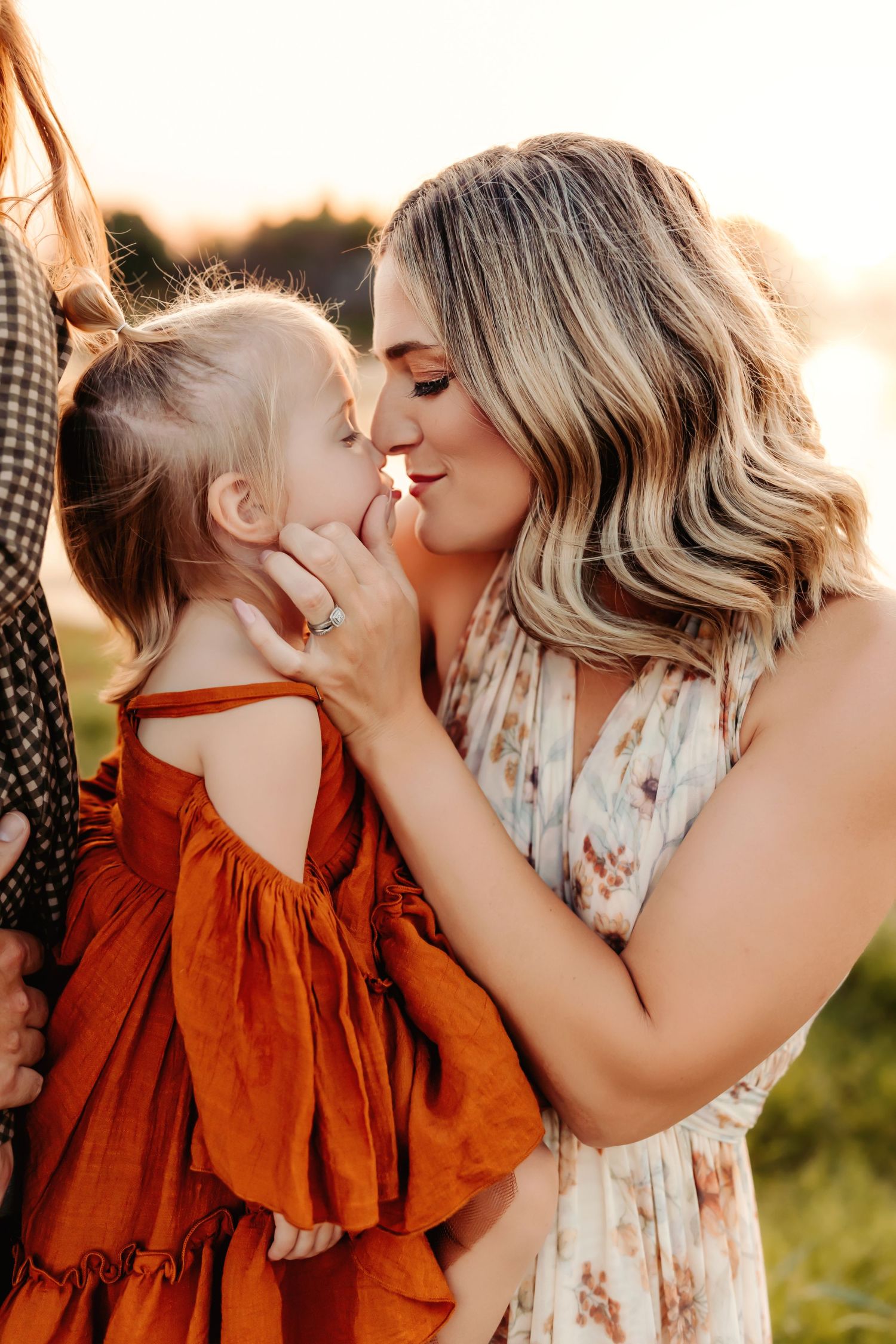 Sweet moment between parent and child in sunset light wearing floral and orange dresses.