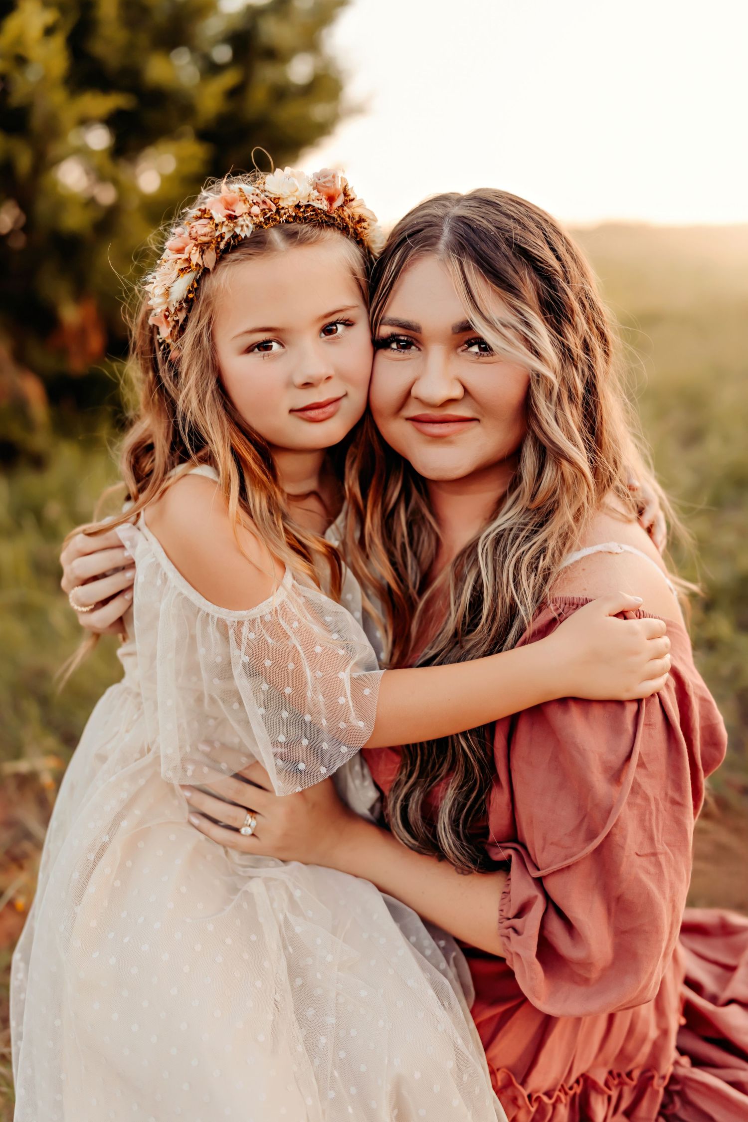 A tender outdoor portrait session at sunset shows warm embraces and matching outfits in dusty rose and cream tones.