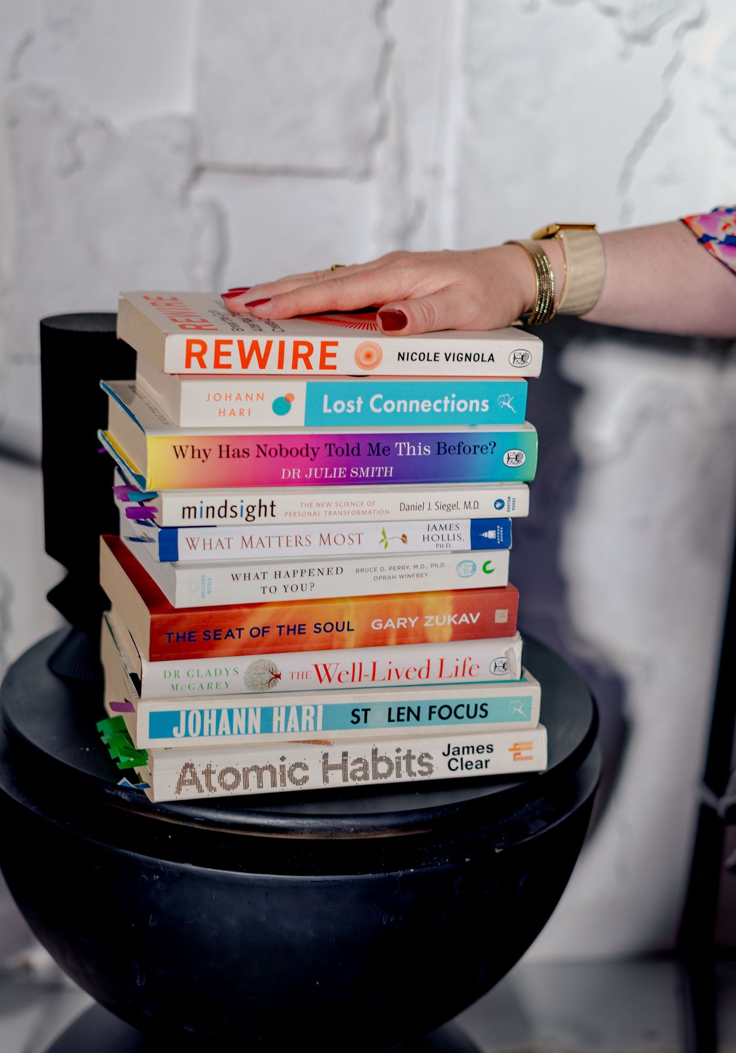 Stack of self-help books including Atomic Habits, Rewire, and Lost Connections on a black bowl table.