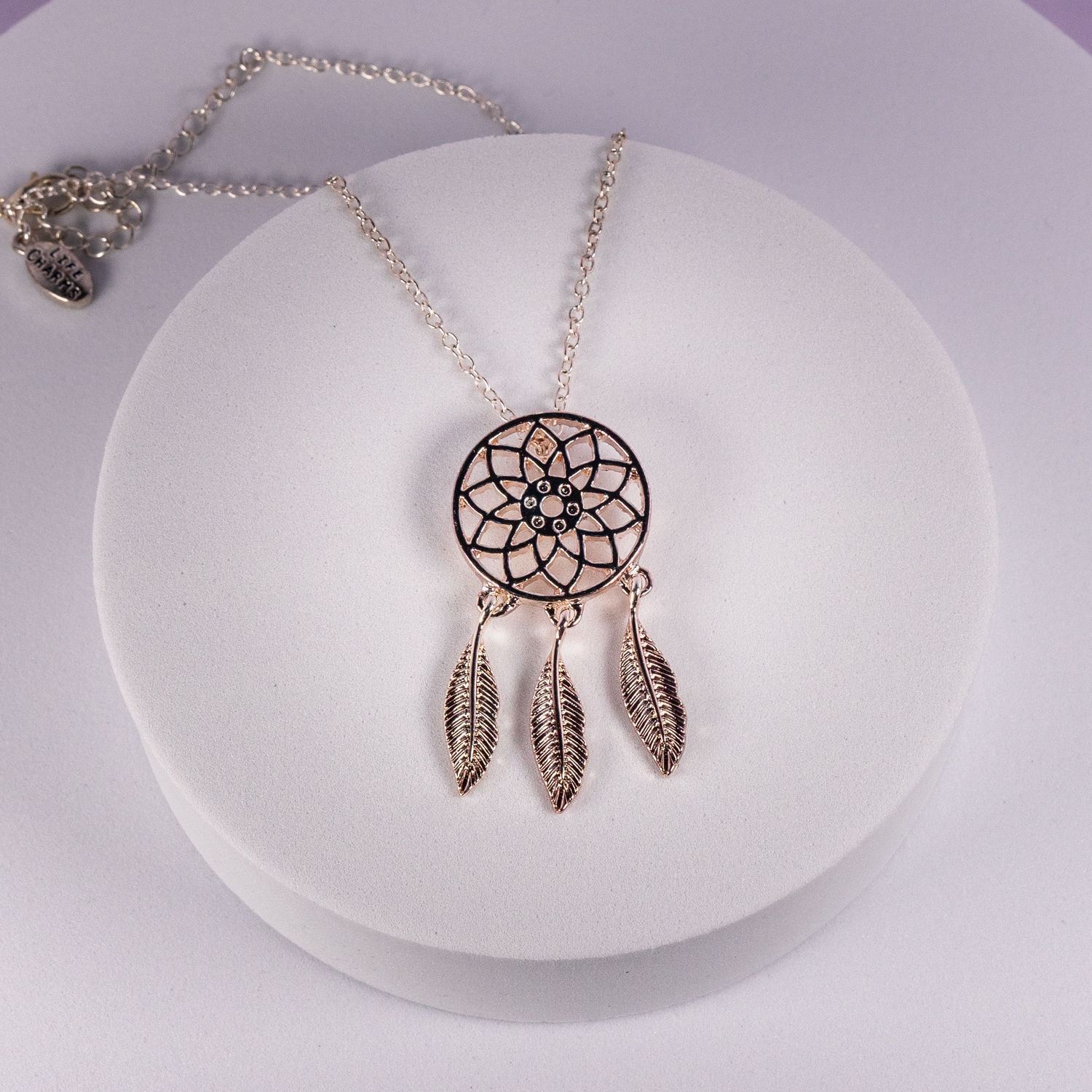 Silver dreamcatcher pendant necklace with feather charms displayed on a white jewelry stand.
