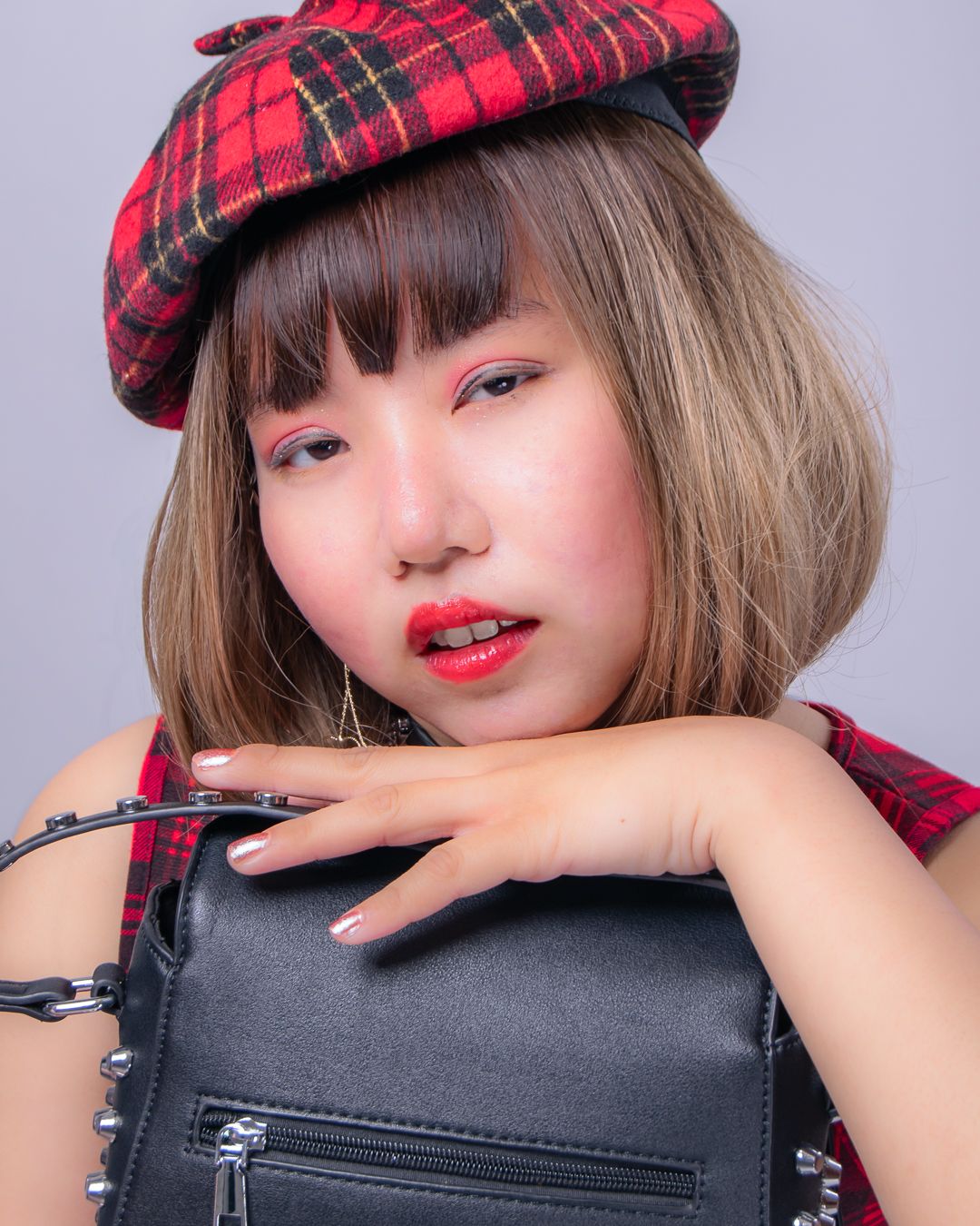 Young woman in red plaid beret and matching outfit, bold red lips, holding black leather bag.