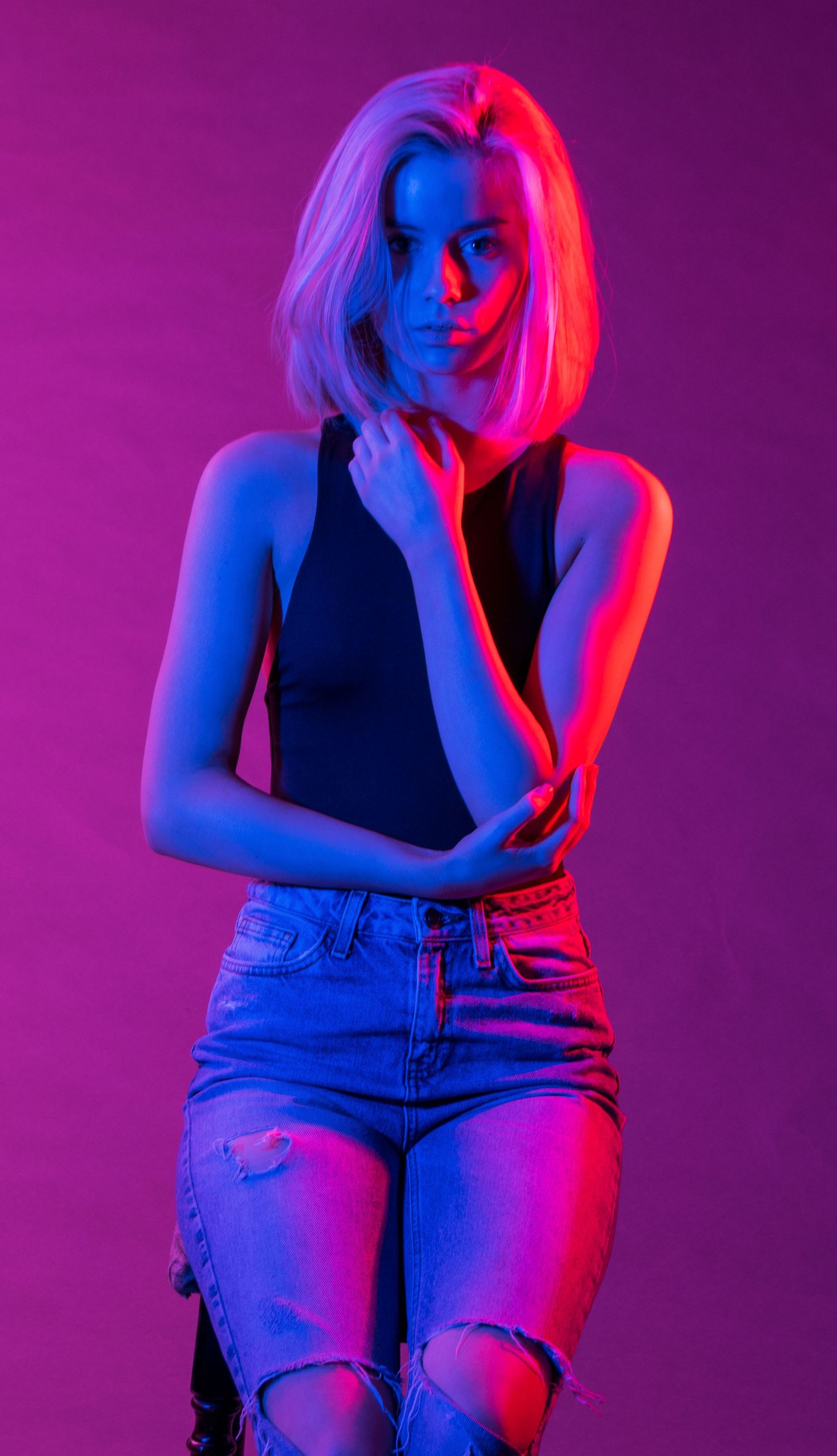 Moody portrait with neon lighting in tank top and distressed jeans.