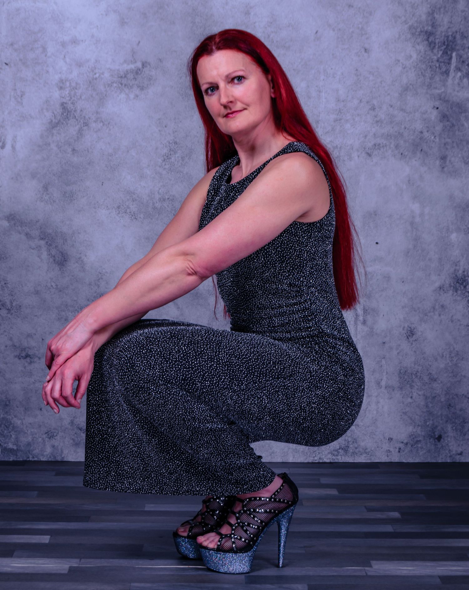 Model in sparkly dress and platform heels poses against grey backdrop.