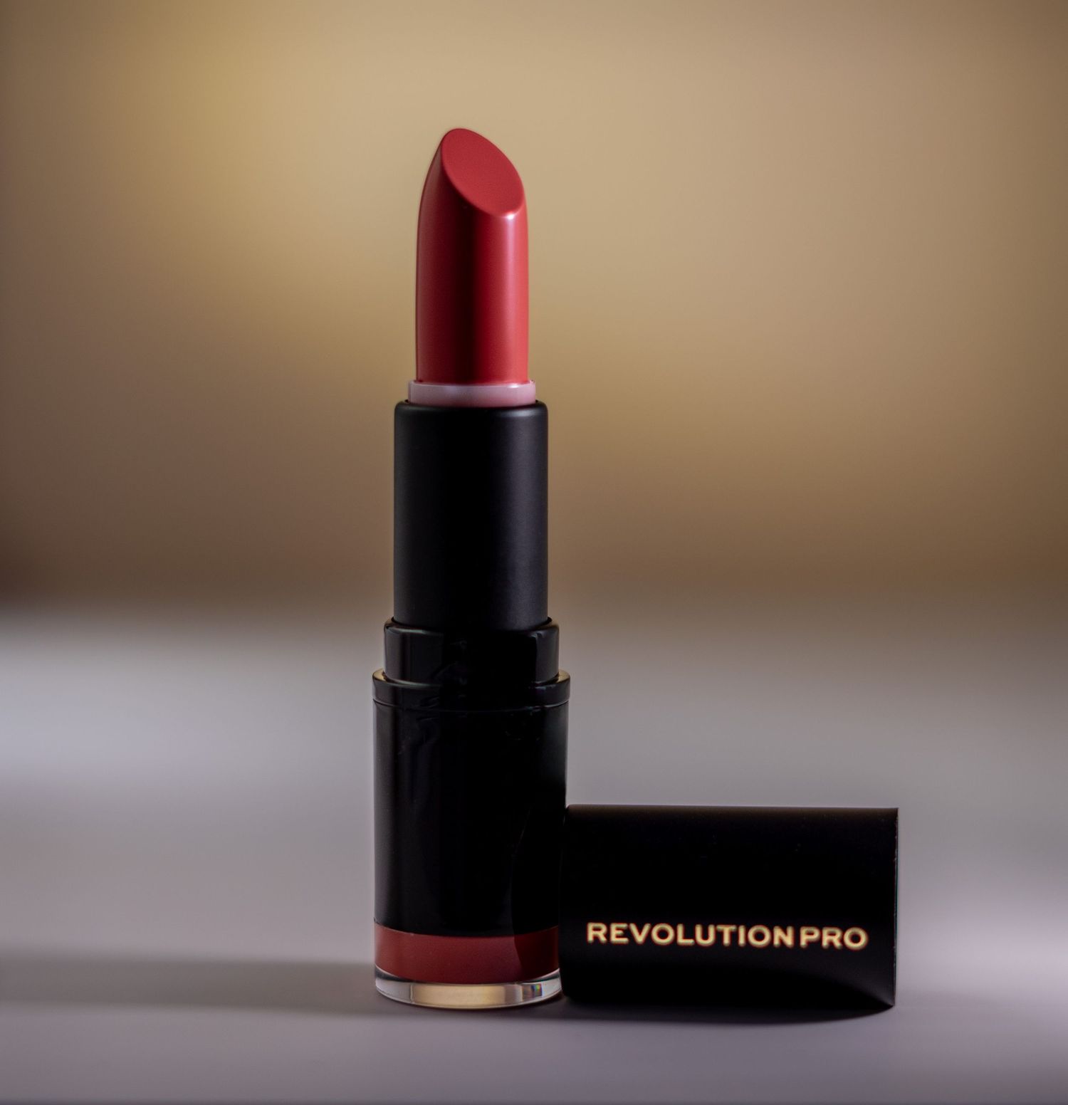 Revolution Pro deep red matte lipstick in sleek black packaging on neutral background.
