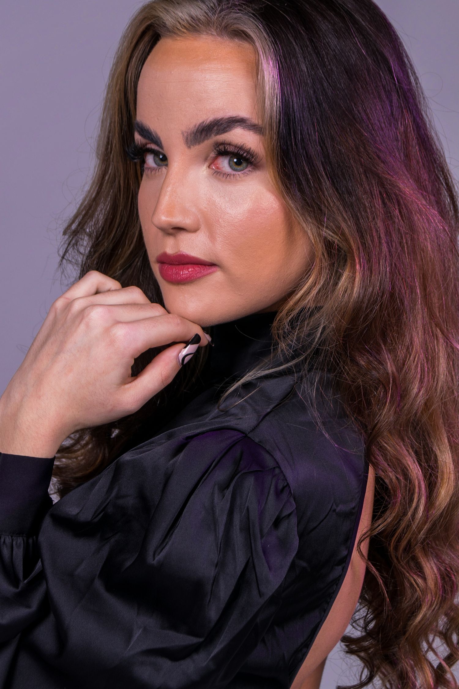 Beauty portrait of model in black top with dramatic lighting against purple background.