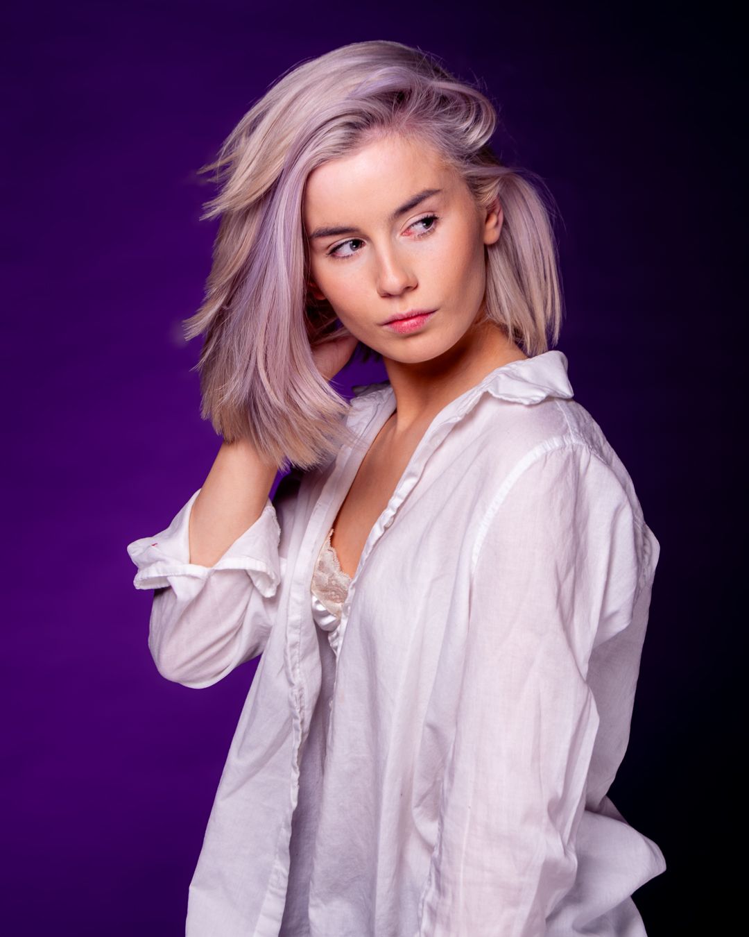 A woman in a white button-down shirt poses against a purple backdrop in a stylish fashion photoshoot series.