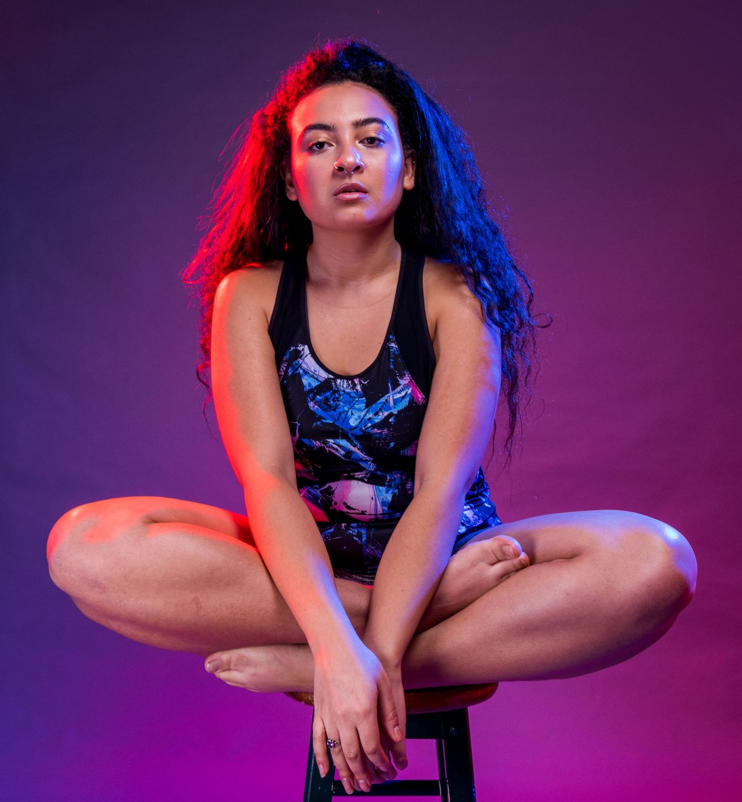 Athletic pose in patterned activewear under dramatic purple and blue lighting.
