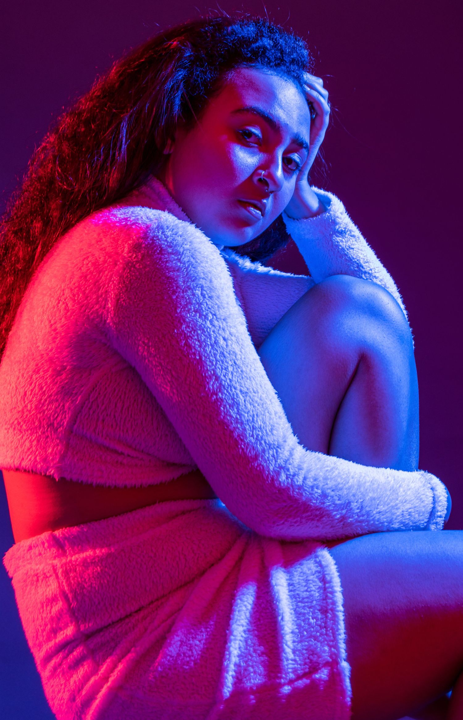 Moody portrait with dramatic red and blue lighting of person in cozy sweater against dark background.