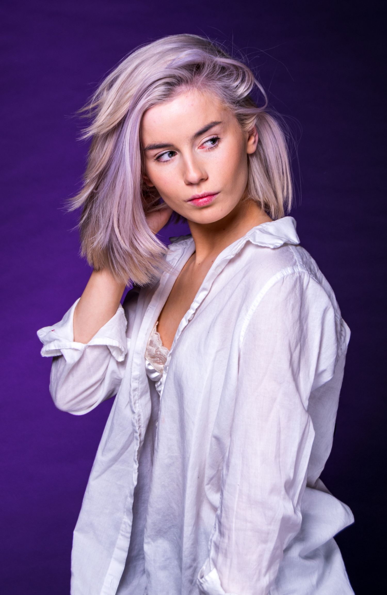 Model in loose white shirt poses dramatically against deep purple backdrop.