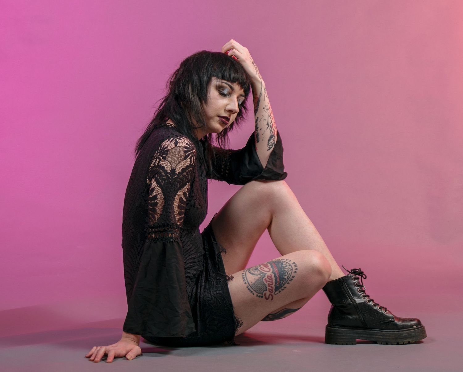 Model in black outfit poses artistically against pink gradient background.
