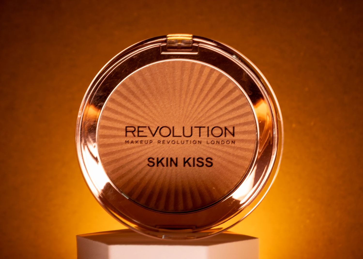 Revolution Makeup London Skin Kiss bronzer compact in rose gold packaging on a golden background.