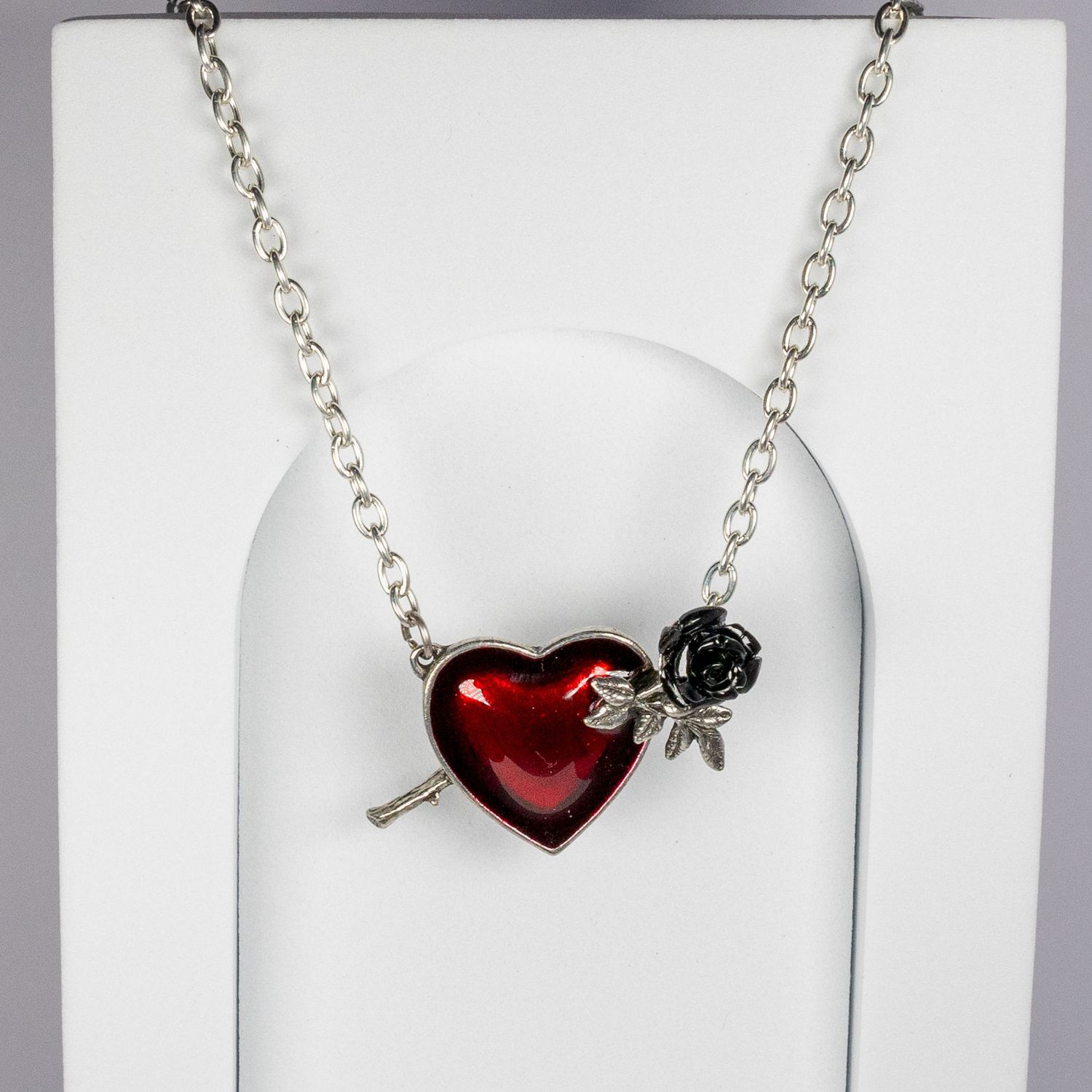 Silver chain necklace with red enamel heart pendant and black rose charm on white display stand.