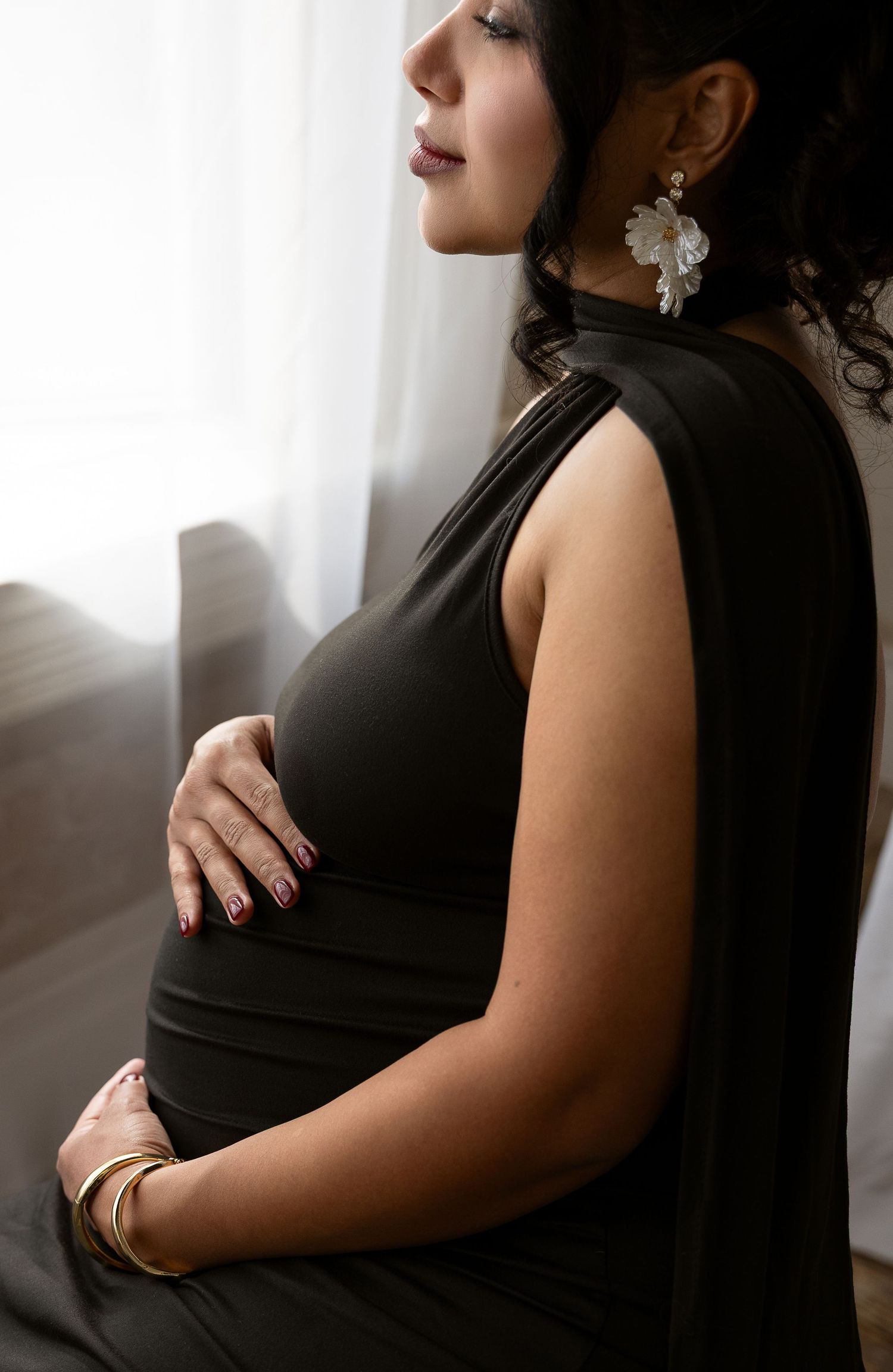 Four artistic maternity photos showing a pregnant woman in a black dress posing against soft window light.