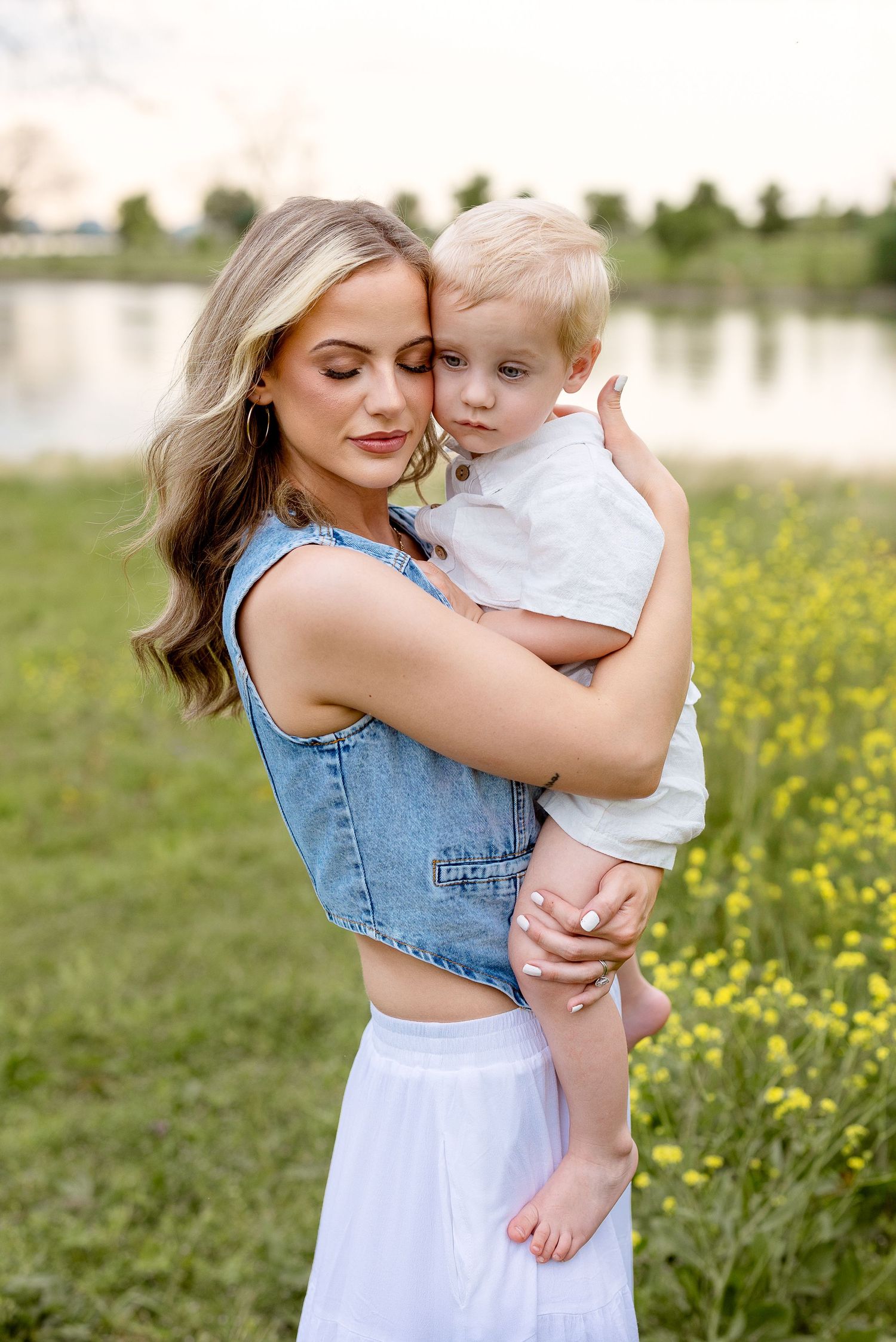 A tender embrace captured outdoors with a lake and yellow wildflowers in the background on a summer evening.