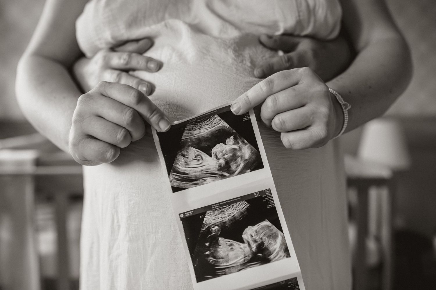 Hands holding a black and white ultrasound photo in a progression of shots showing it being revealed.