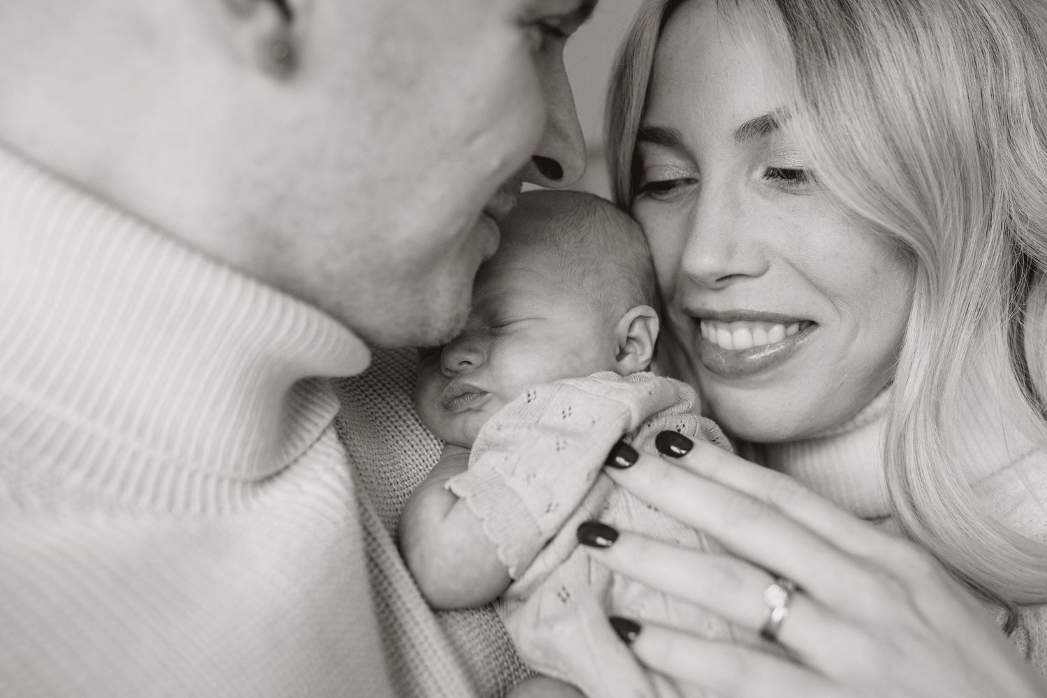 A tender black and white portrait of parents sharing a joyful moment with their newborn baby.