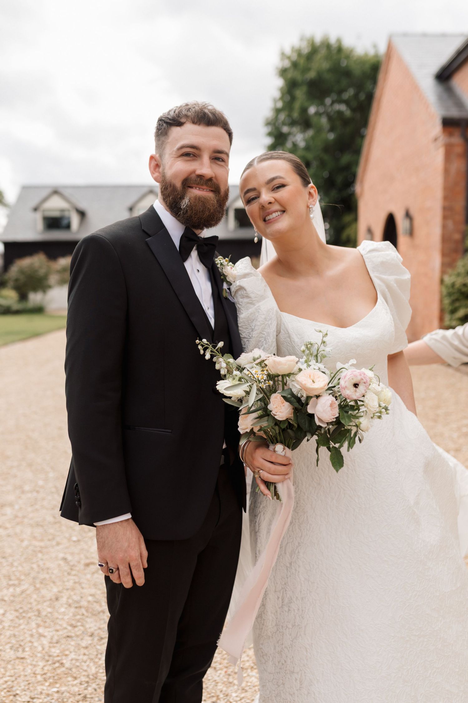 A happy couple poses together on their wedding day, with the bride holding a soft pink and white floral bouquet.