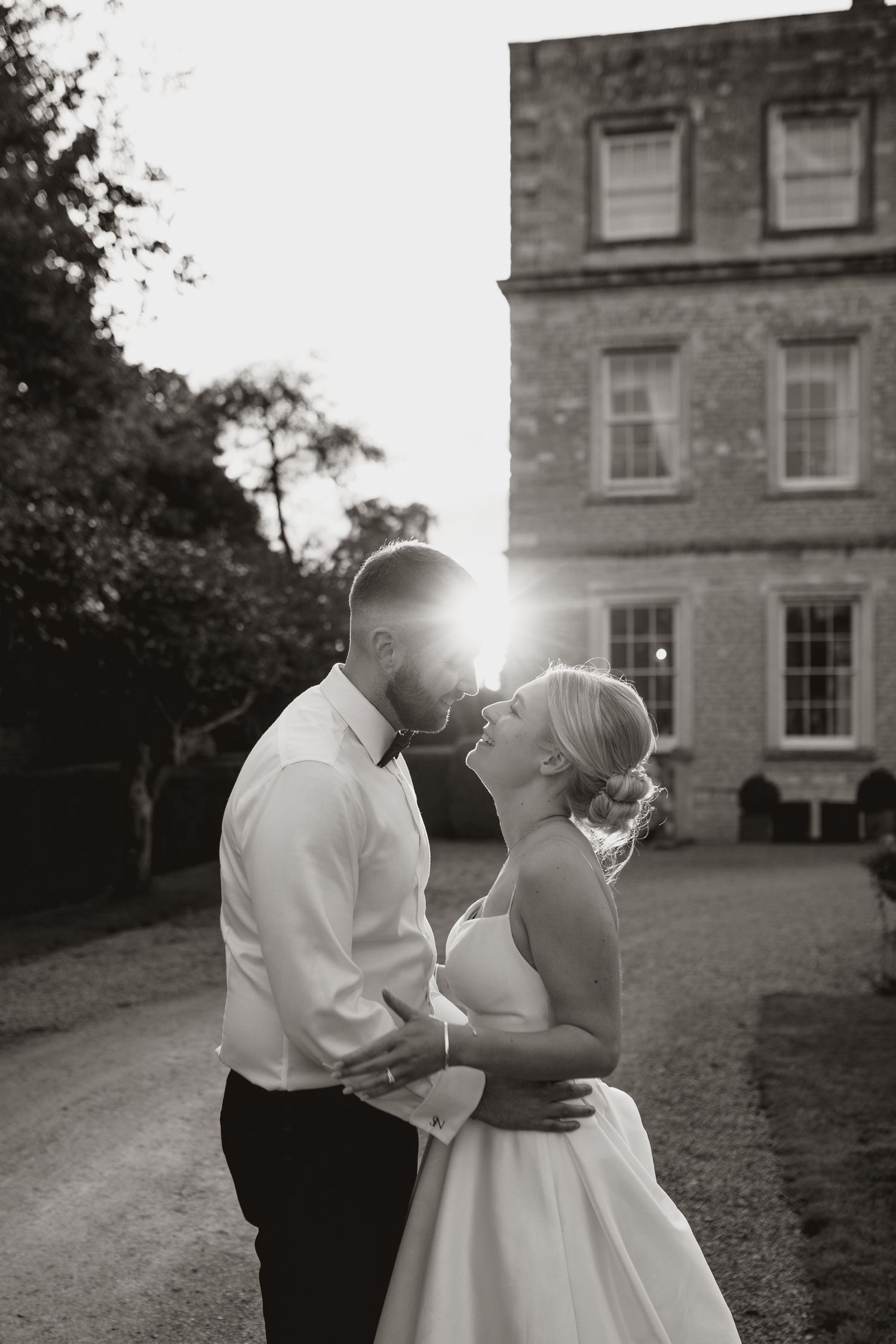 A romantic black and white photo series of a couple in wedding attire sharing intimate moments outside a stately manor house.