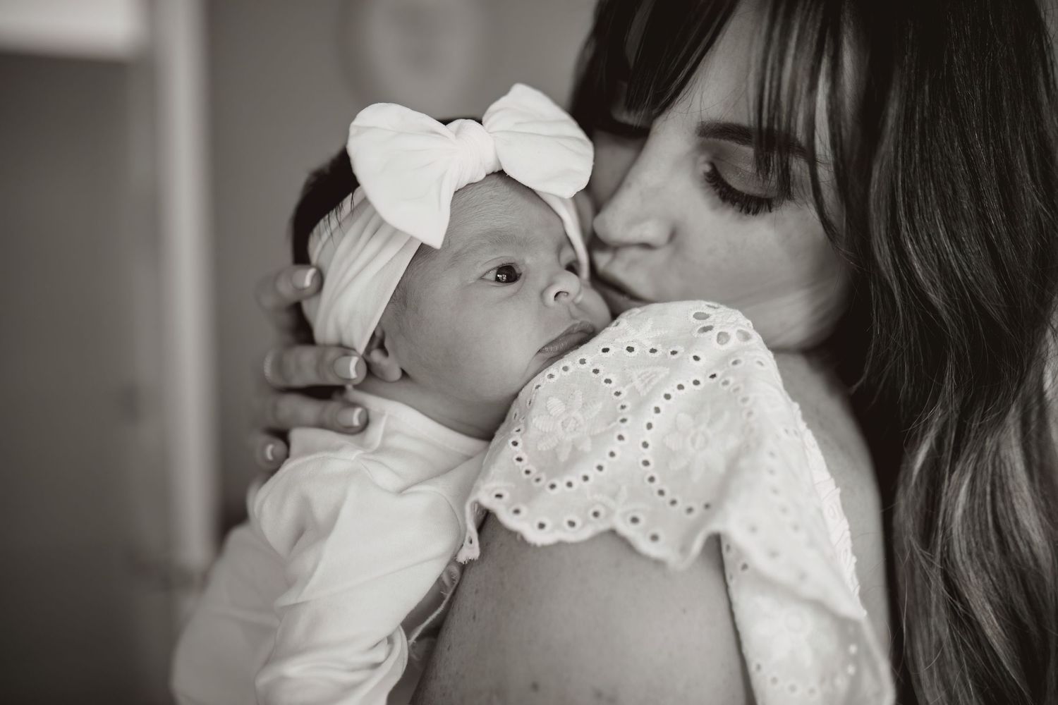 A series of six black and white photos showing intimate moments between a parent and baby in white clothing.