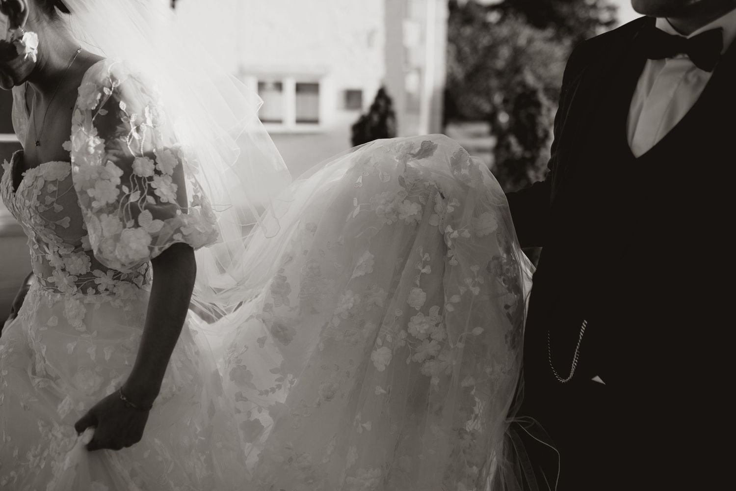 Black and white photograph capturing the details of a wedding dress and tuxedo.