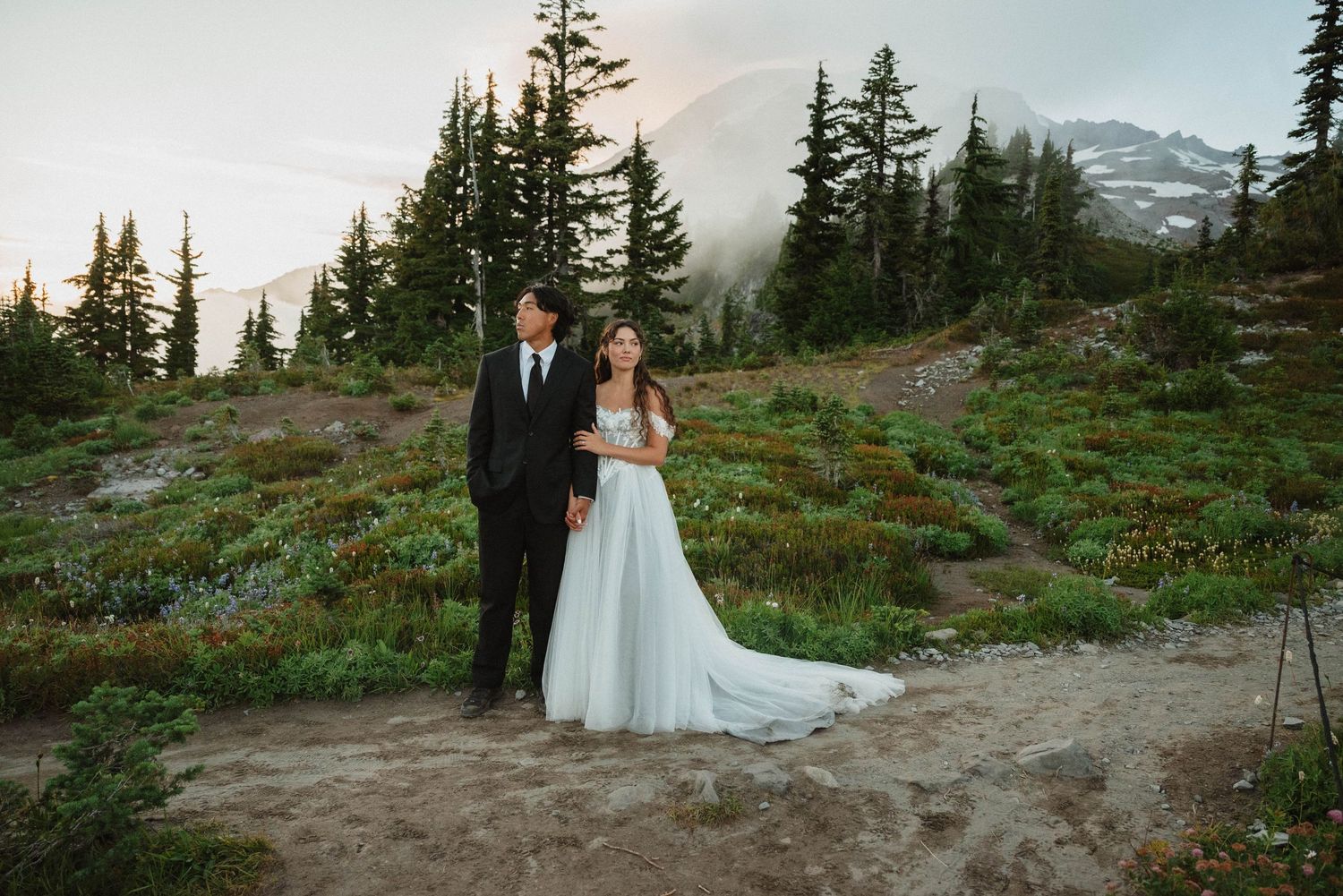 Bride and groom posing in front of Mount Rainier as it peaks out of the fog in Mount Rainier National Park