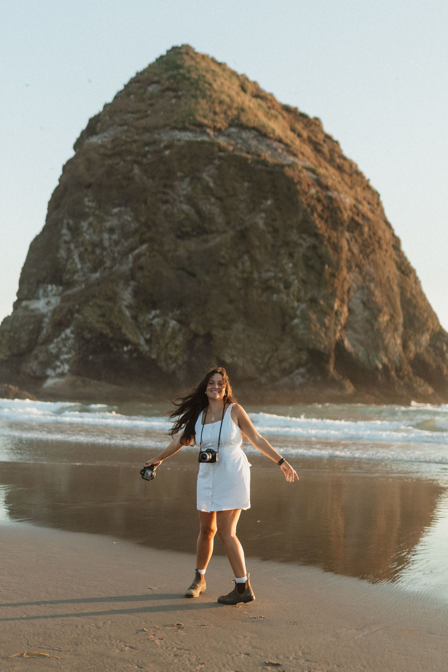 photographer laughing and spinning in front of Haystack Rock on Cannon Beach, Oregon
