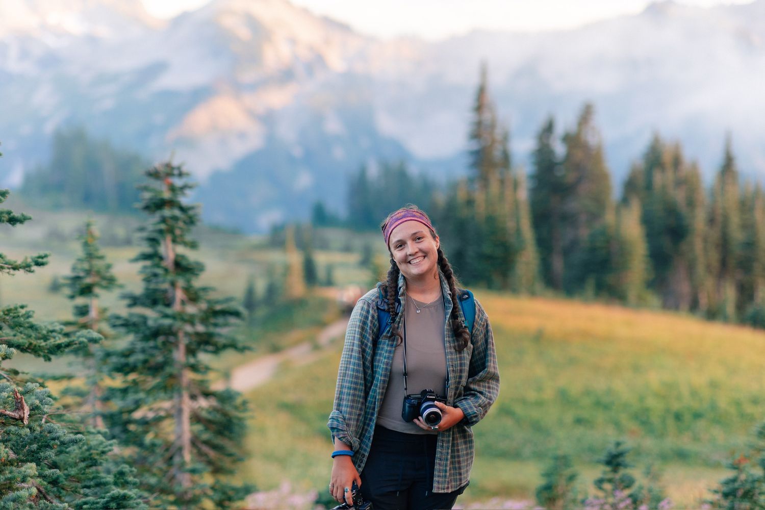 photographer with a camera smiling in front of Tatoosh Mountain range in Mount Rainier National Park
