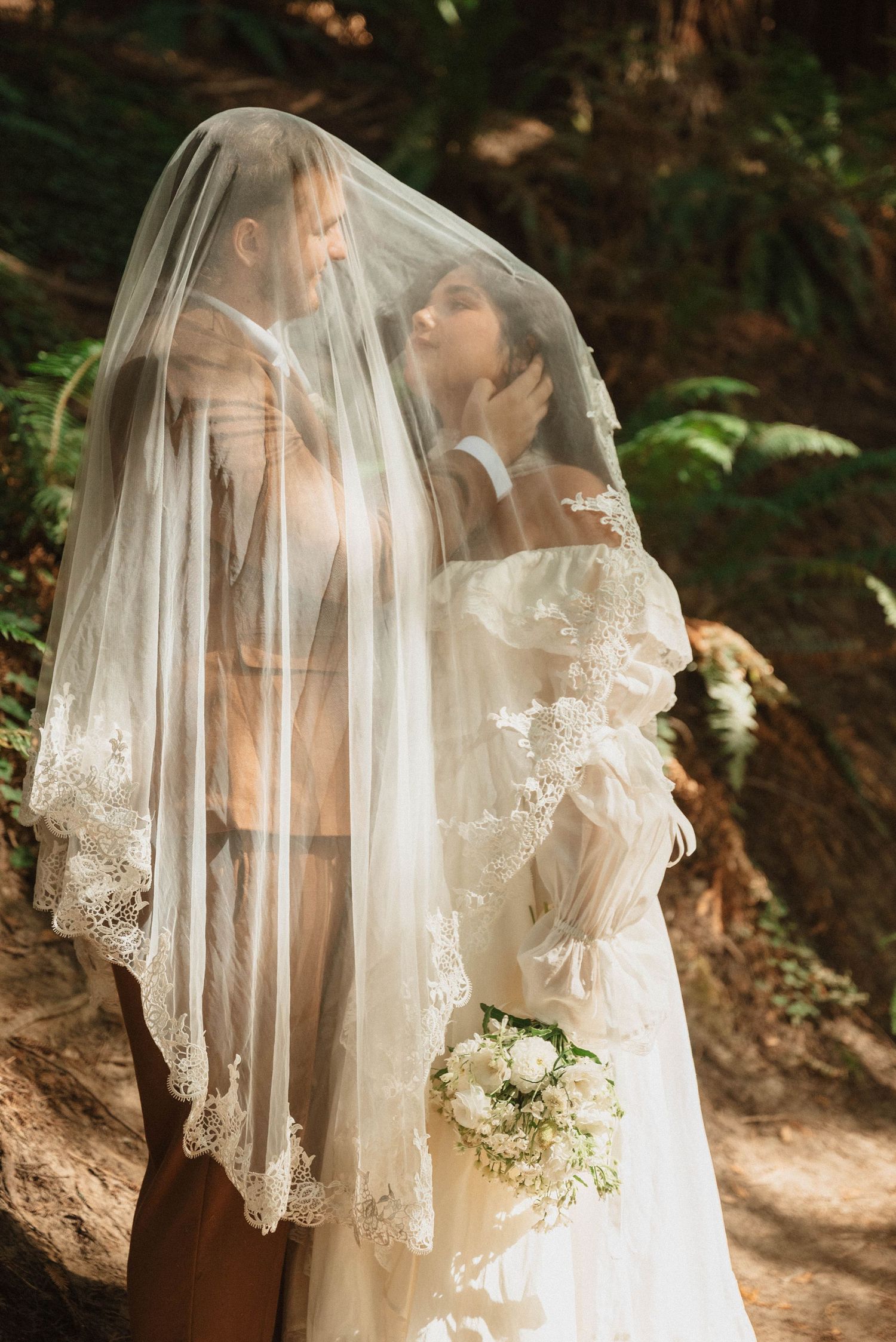 Bride and groom leaning in for a kiss under a veil among the tall redwoods at Hoyt Arboretum in Portland, Oregon.