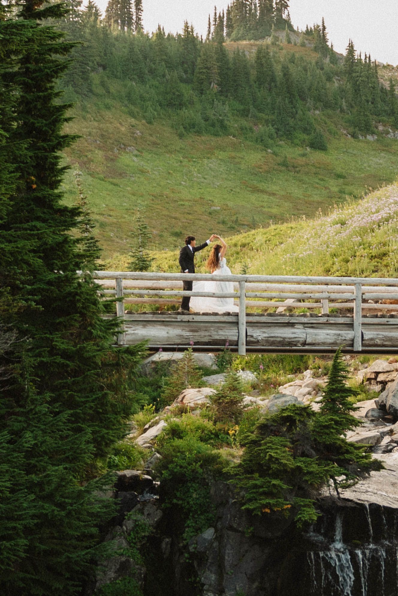 Bride and groom dancing on a wooden bridge above Myrtle Falls during their Mount Rainier National Park elopement at golden hour.