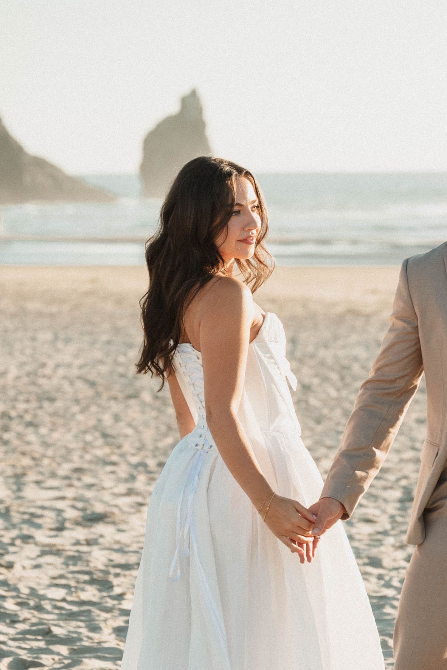 Bride holding her her grooms hand on the beach at her Cannon Beach elopement in Oregon