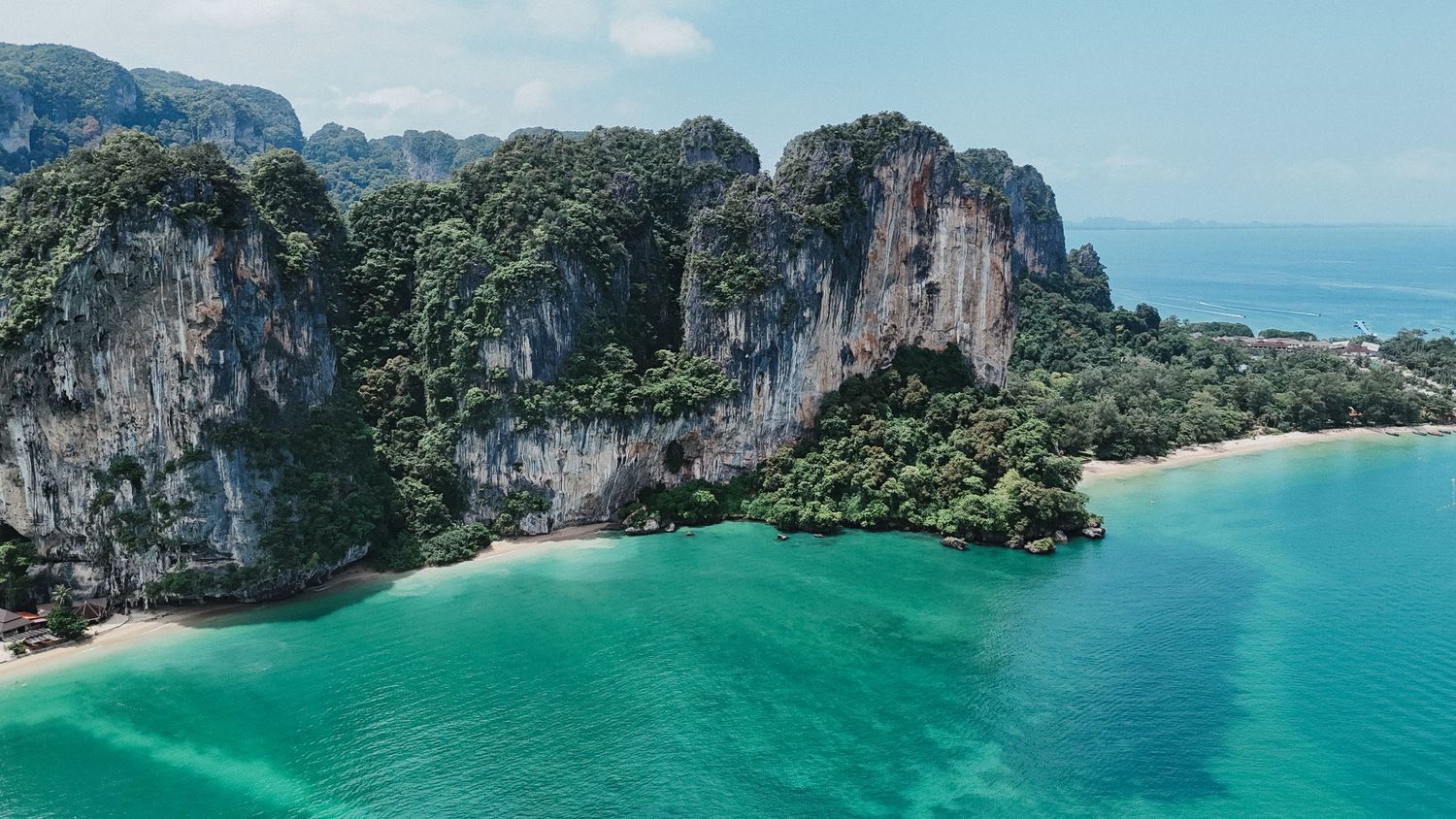 Aerial view of dramatic limestone cliffs and lush jungle meeting turquoise waters at Railay Beach, Thailand.