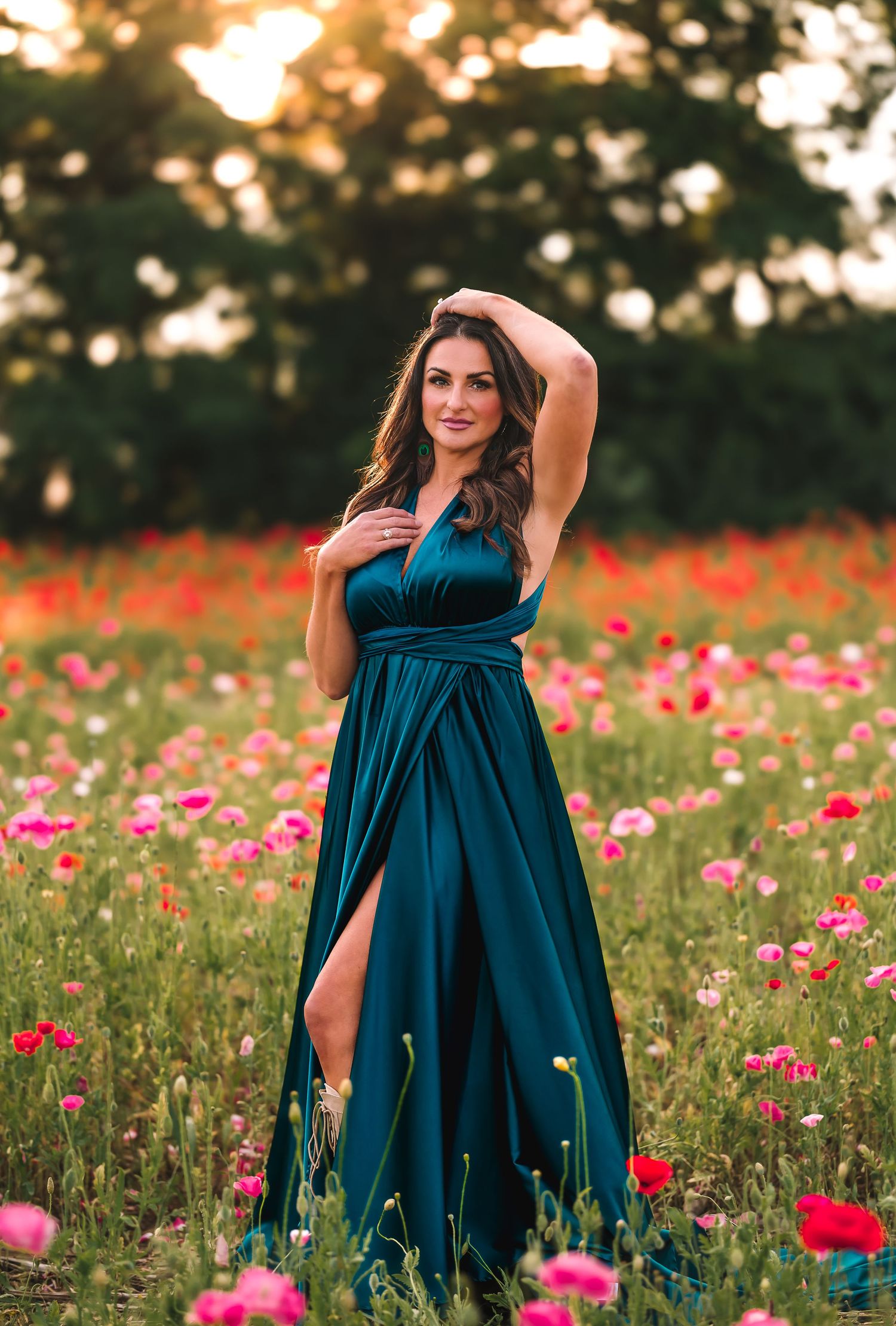 Elegant teal evening gown dress slit in field of pink and red poppy flowers at golden sunset.