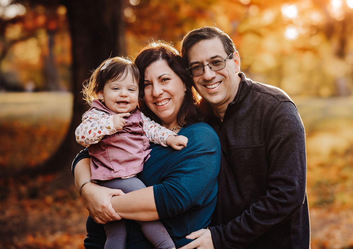 A joyful family portrait with autumn foliage in the background during golden hour.