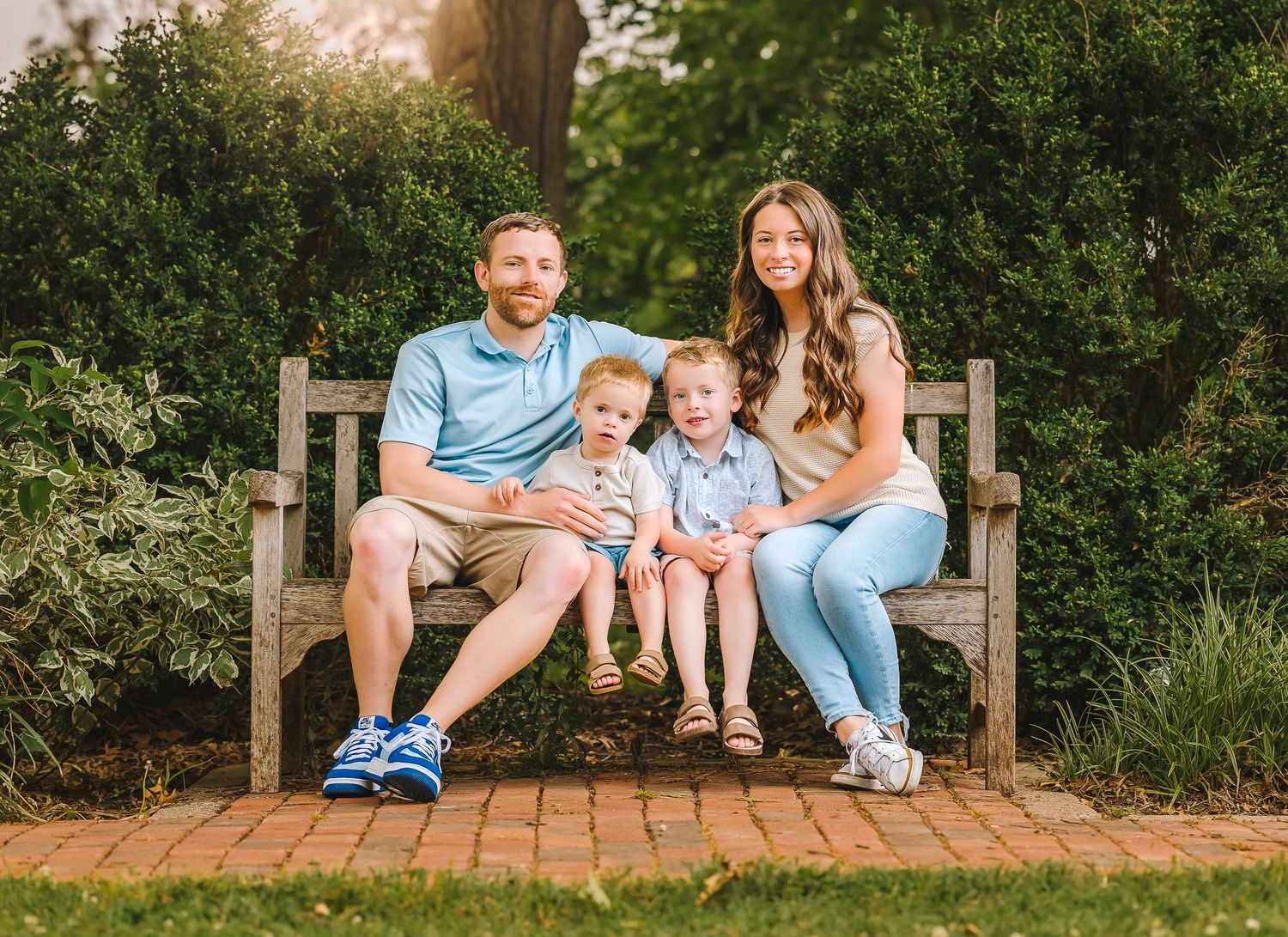 A family relaxing together on a wooden bench in a garden setting during golden hour sunset.
