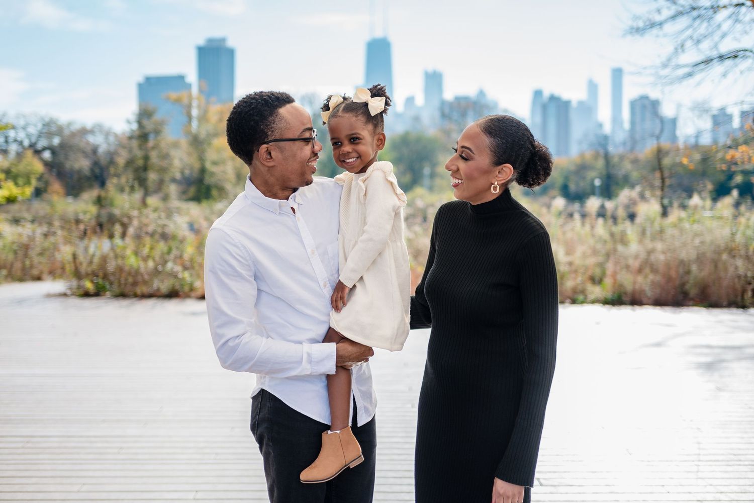 Family of three posing on a wooden dock with Chicago skyline in the background on a fall day.