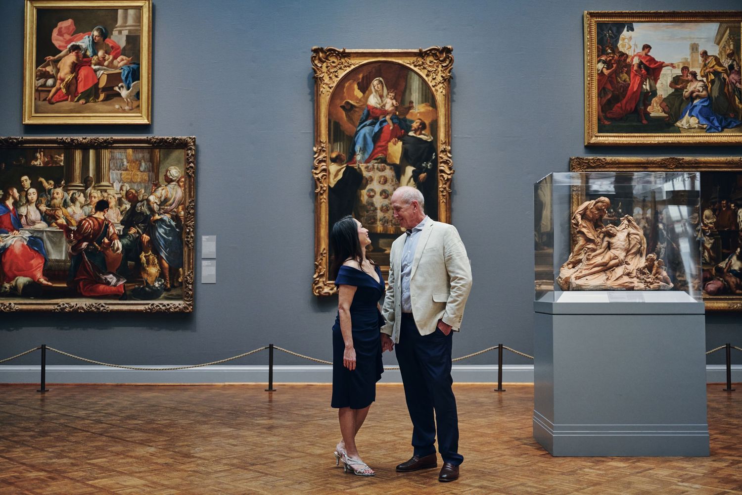 Couple sharing a romantic moment in an art museum surrounded by classic Renaissance paintings and sculptures.