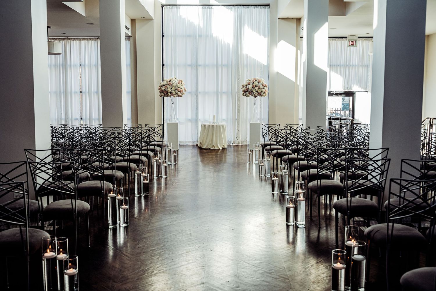 Elegant wedding ceremony venue with rows of dark chairs, candle lanterns lining the aisle, and floral arrangements at the altar.