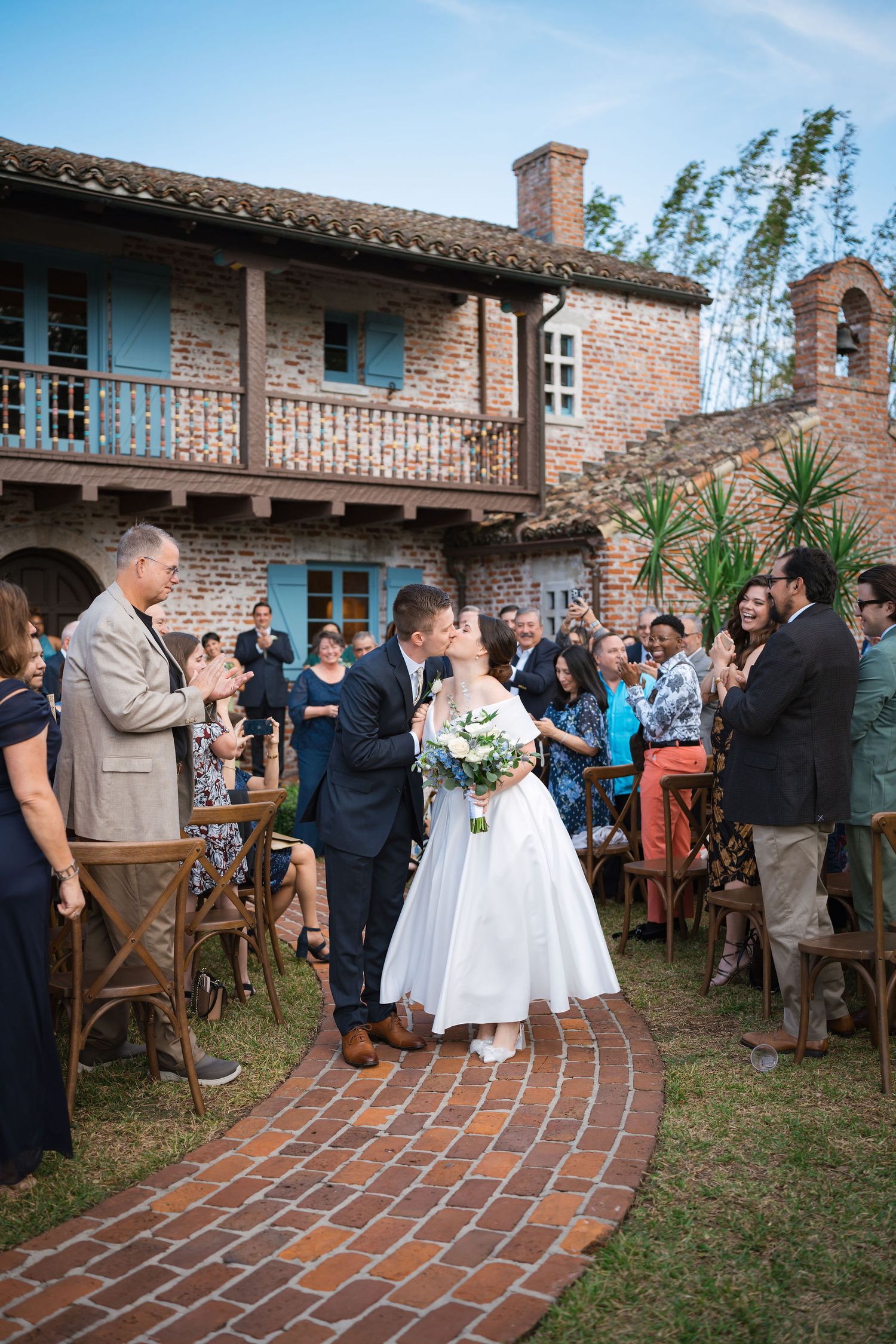 A sequence of candid moments at a rustic outdoor wedding ceremony shows guests gathered on a brick patio near a Spanish-style building.