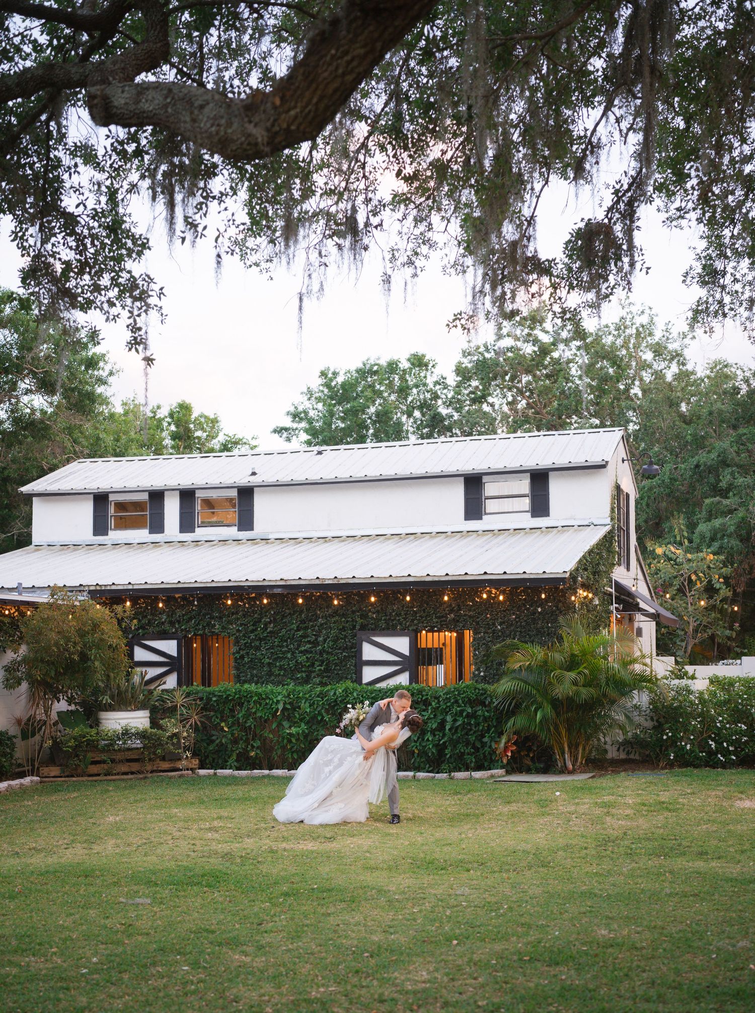 Wedding reception area in rustic barn venue with string lights and sprawling green lawn at dusk.