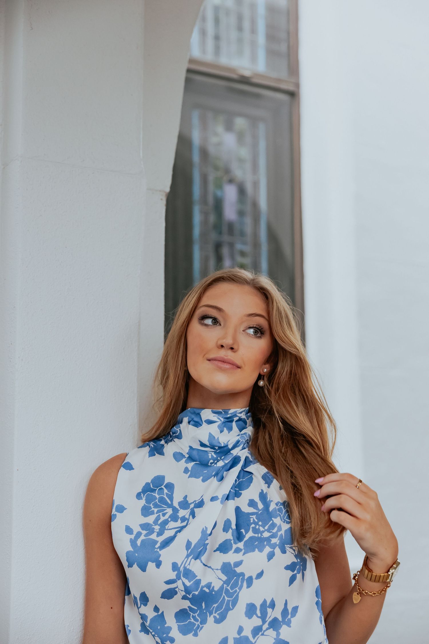 A portrait of someone wearing a blue and white floral sleeveless top against a white architectural backdrop.