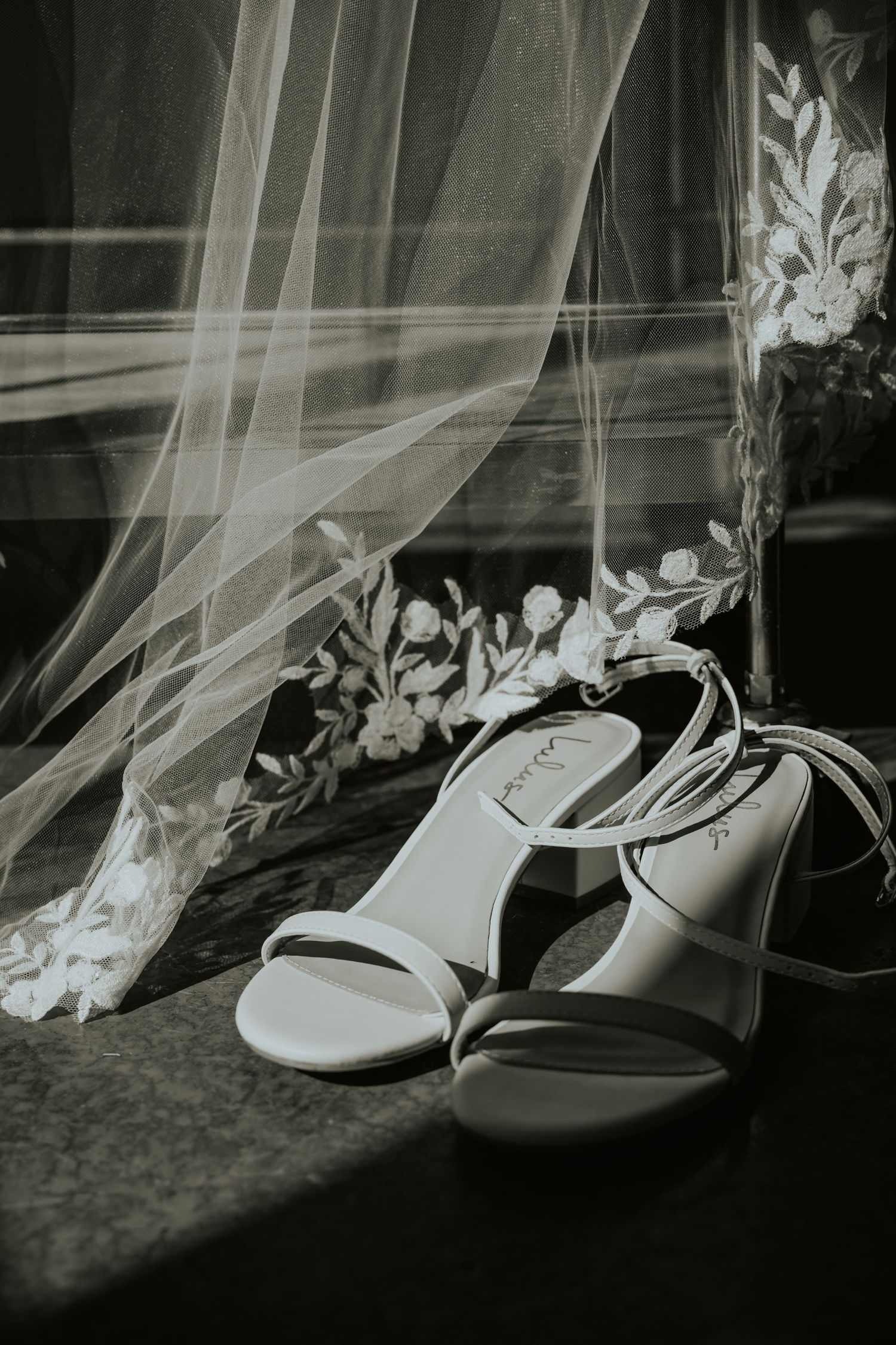 White wedding shoes with delicate lace veil details in a dark artistic composition.