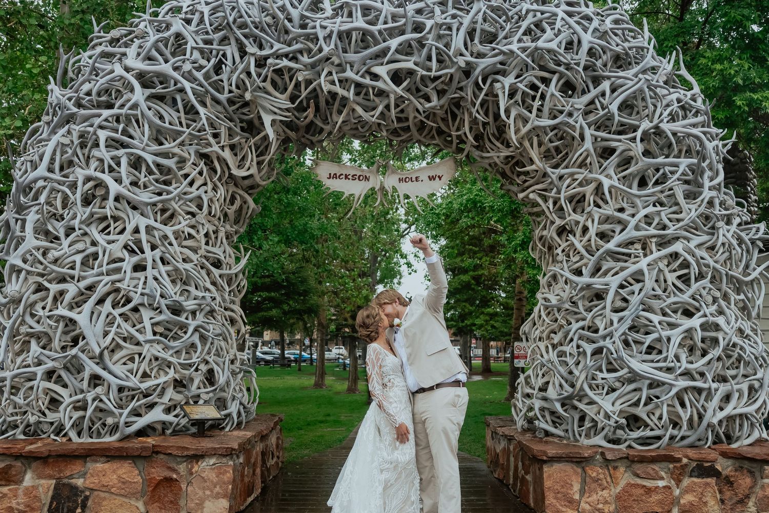 Wedding couple poses under decorative white arches in a garden setting.