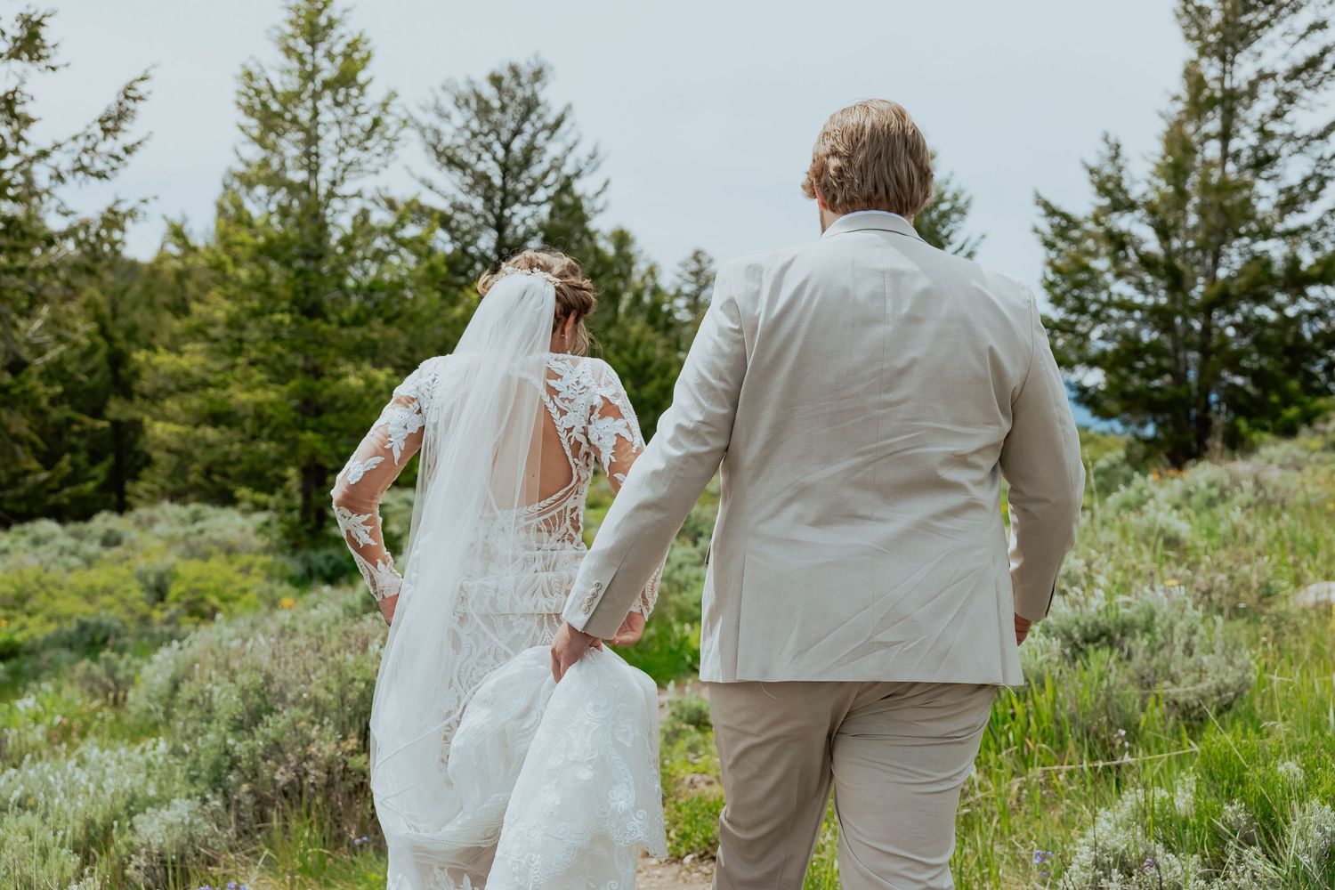 Wedding couple walking along a scenic mountain path surrounded by evergreen trees and natural beauty.